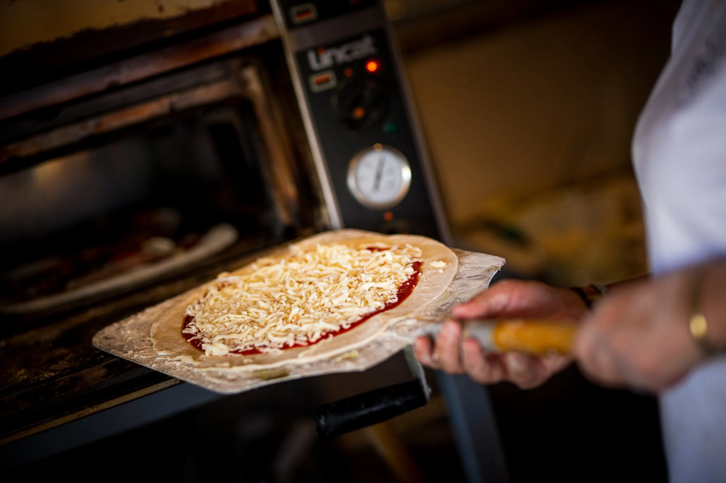 Person placing a pizza with cheese and tomato sauce into an oven.