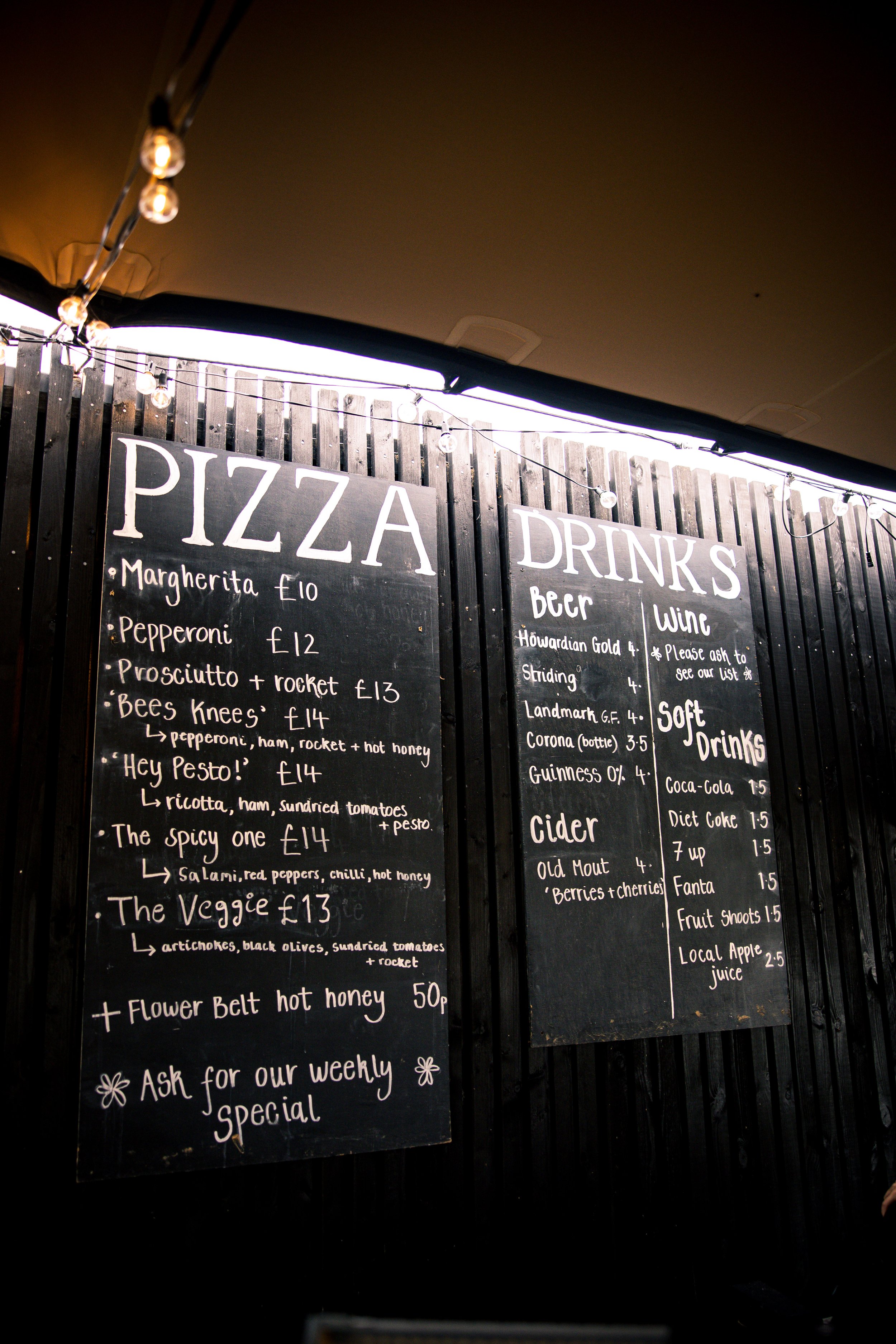 Menu board with various pizza options and prices, drink selections including beer, wine, and soft drinks, all written on blackboards.