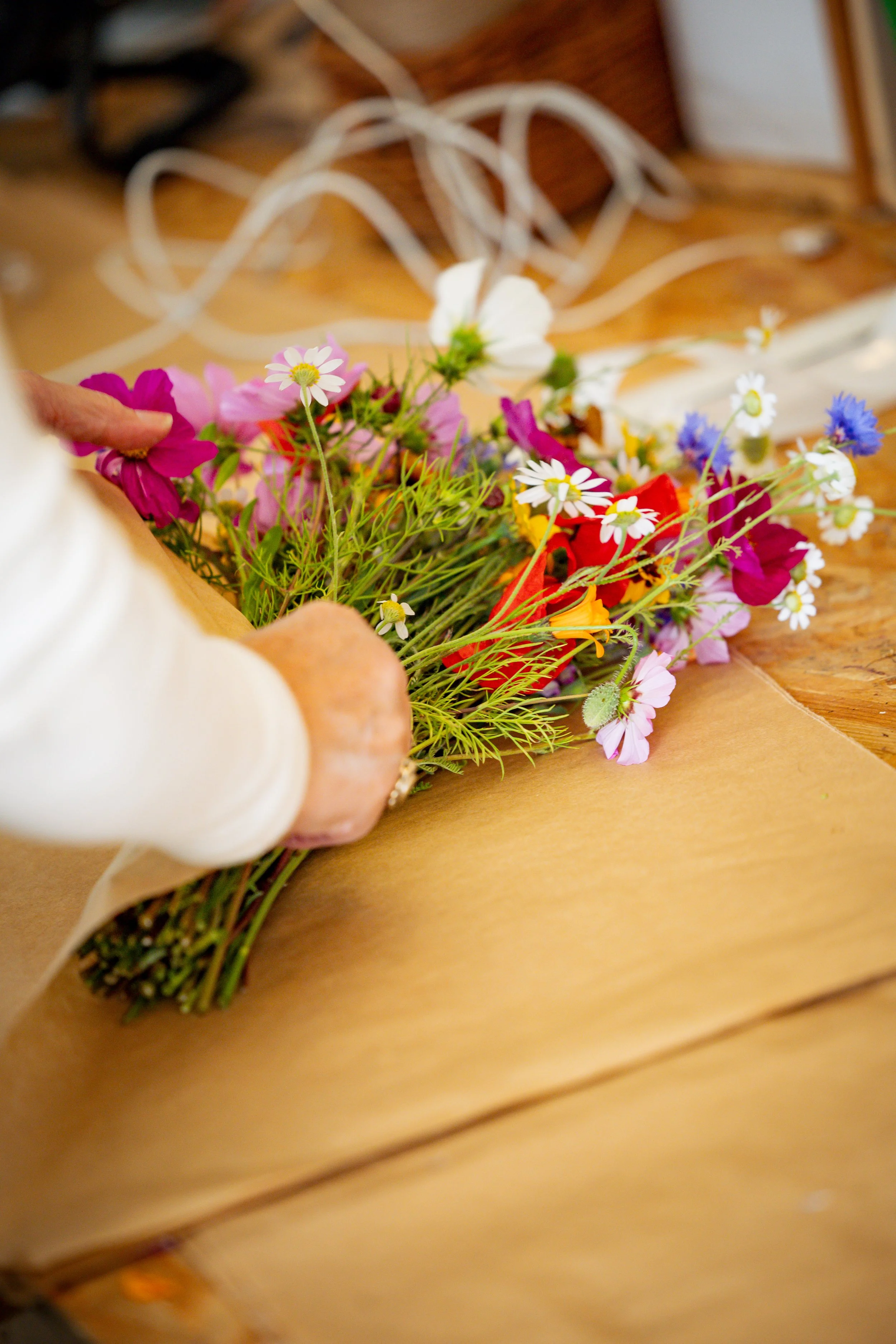 A person holding a bouquet of colourful wildflowers that are partially wrapped in brown paper.