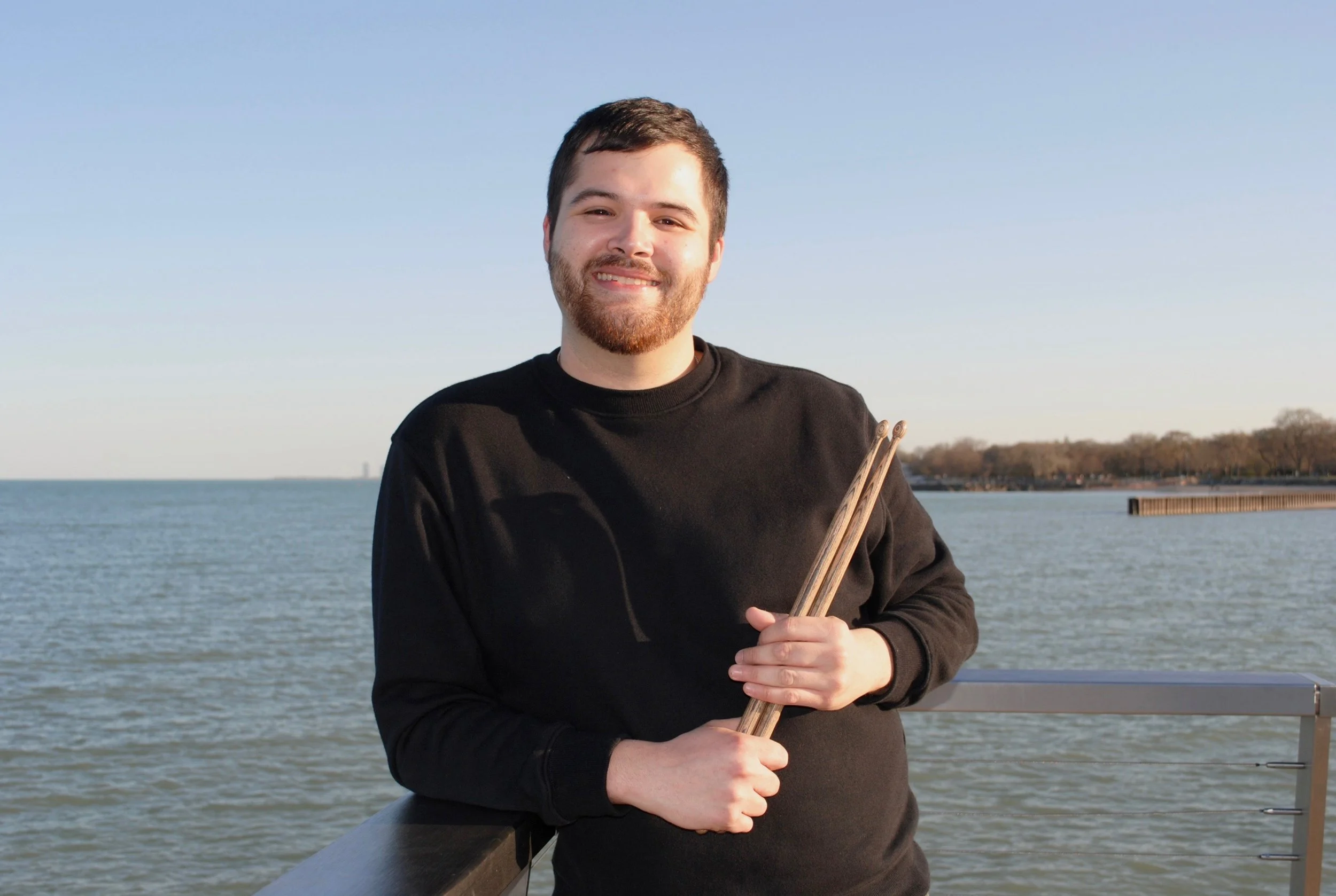 Man holding drumsticks by a lake