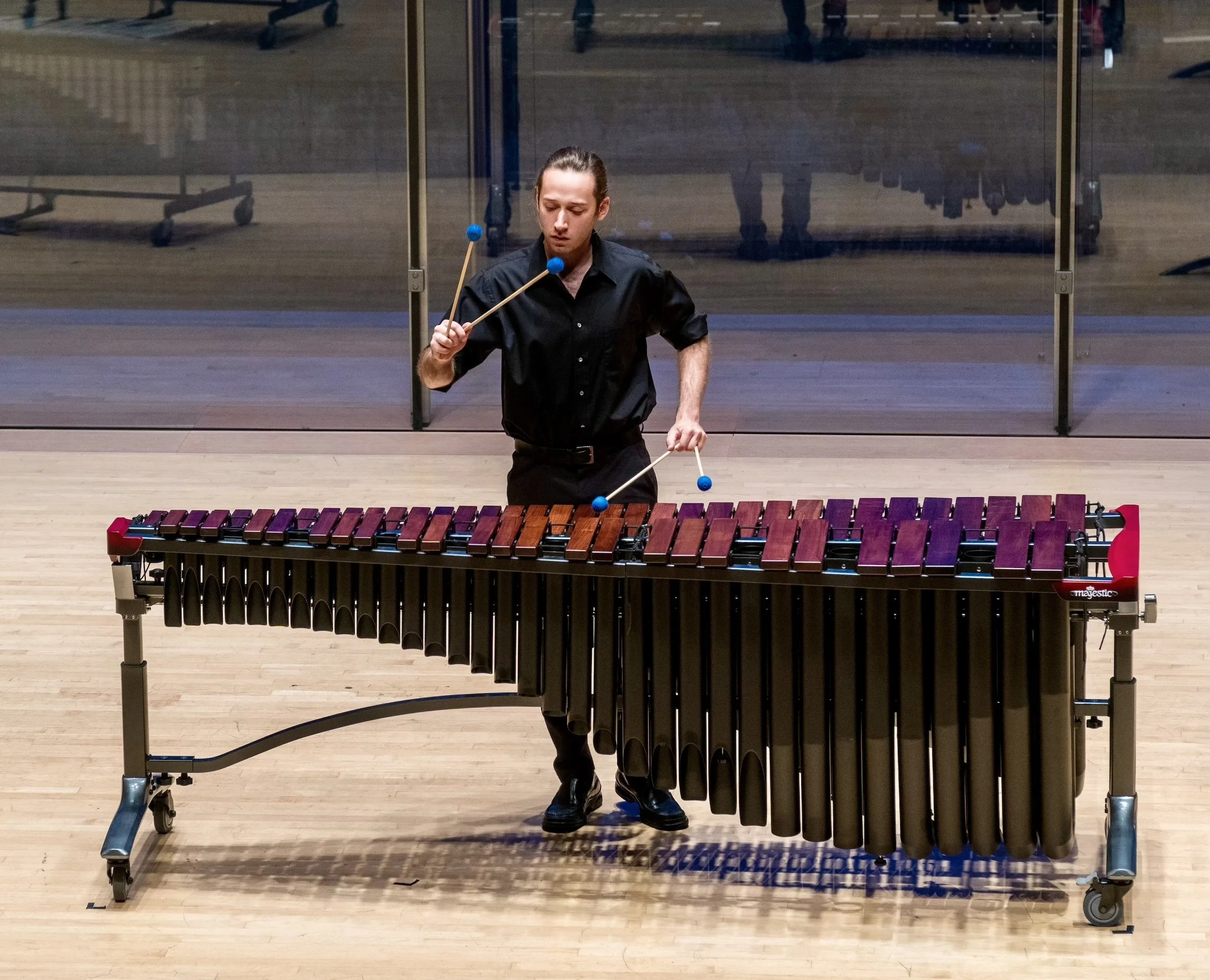 A person with long dark hair is smiling, wearing round glasses and a black lace top against a dark background.