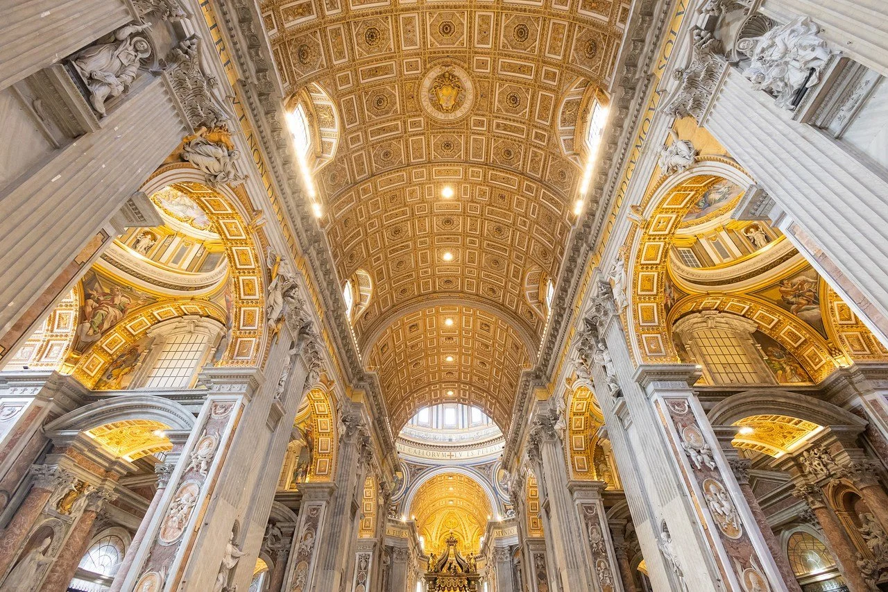 Interior view of a large ornate church or cathedral with a gold decorated ceiling, tall columns, and detailed sculptures.