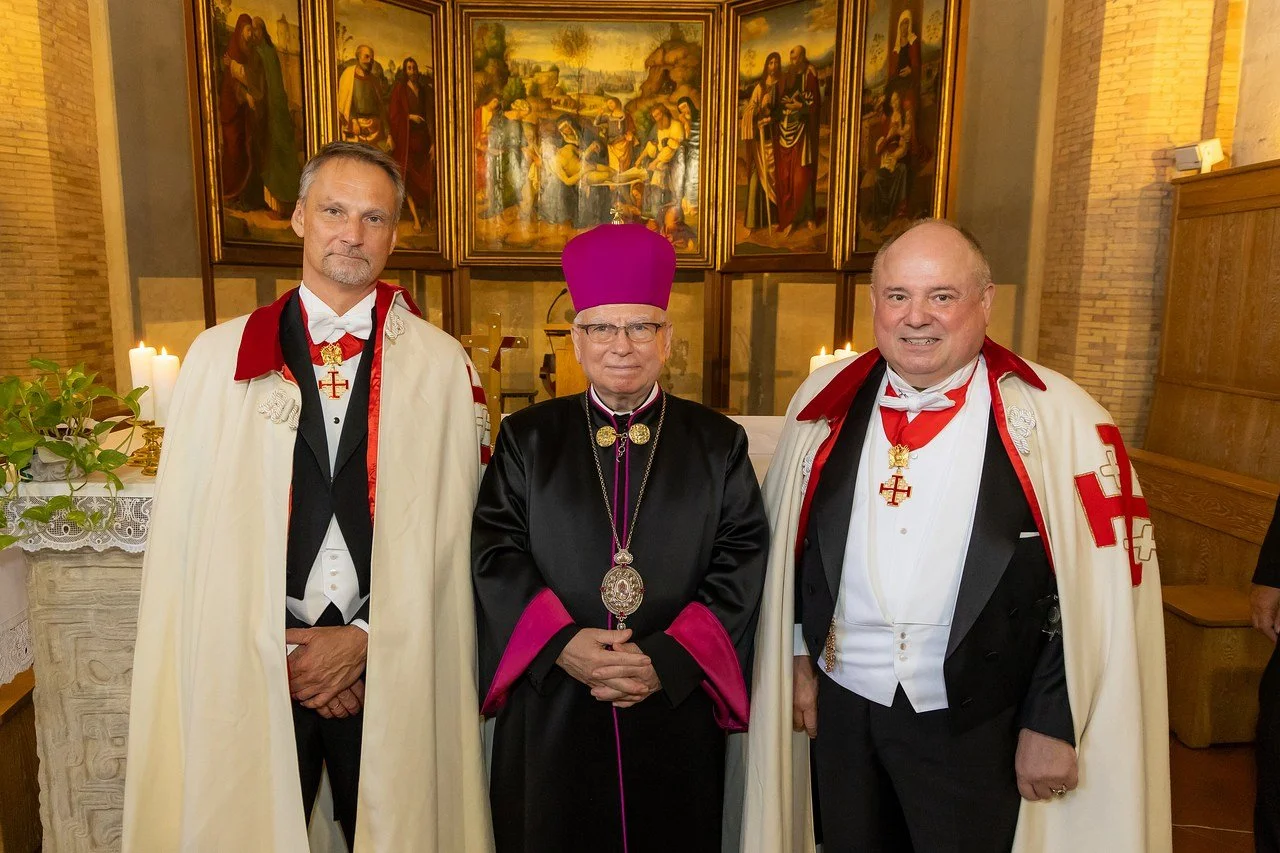 Three men in ceremonial religious robes standing inside a church with religious paintings and candles in the background.