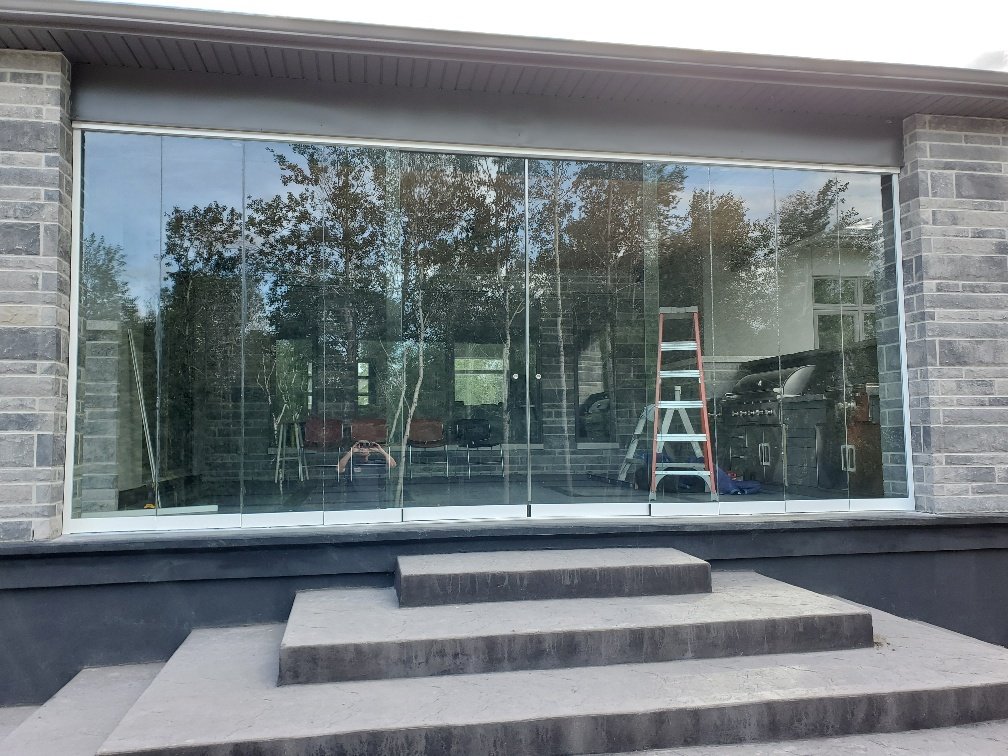 Large glass doors with metal frames on a modern building, reflecting trees and a red ladder inside.