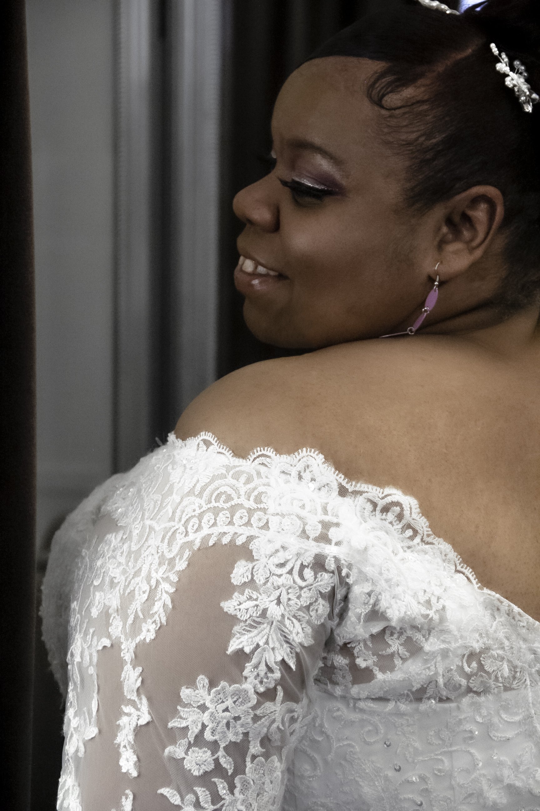 Bride in lace wedding dress smiling, with side profile view.