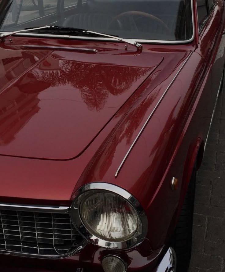 Close-up of a vintage red car with a chrome headlight and grille.
