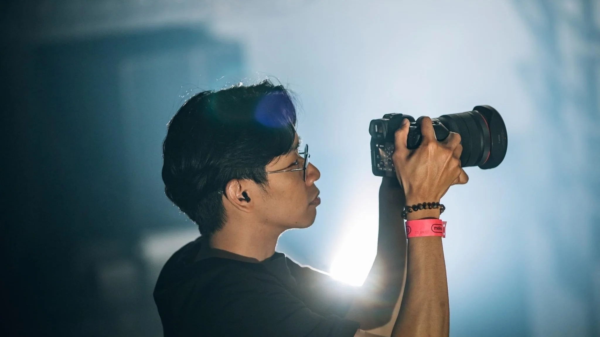 Person holding a camera, focusing intently, with a wristband and dark hair in a dimly lit environment.