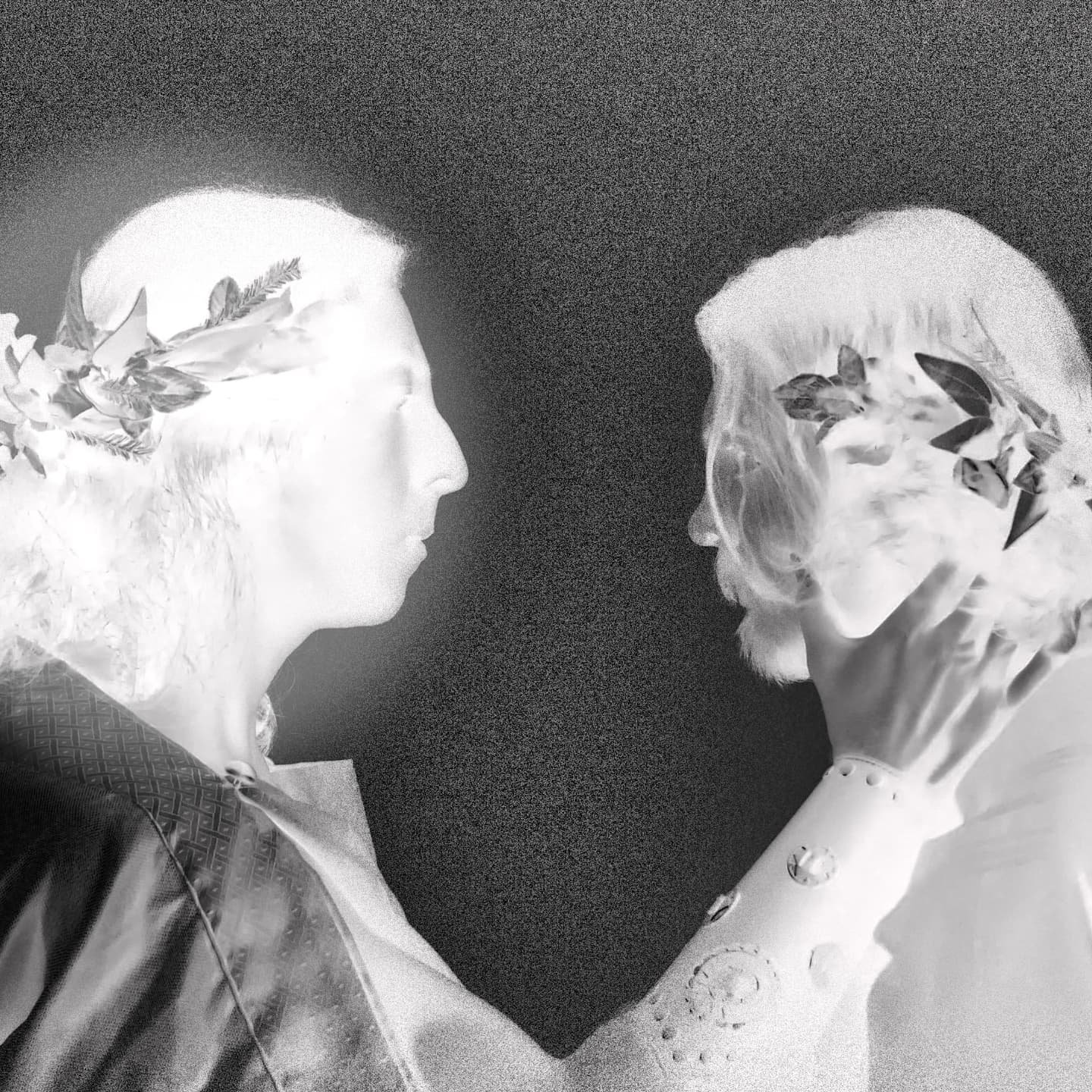 Inverted image of two people in profile facing each other, wearing laurel crowns and historical clothing.