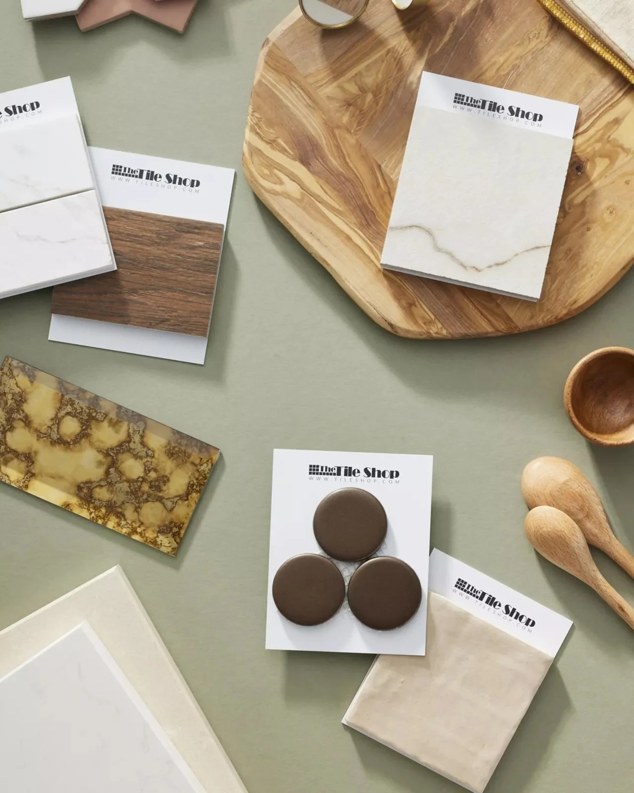 Various tile samples on a table, including marble, wood, and decorative pieces, organized around wooden utensils and a tray.