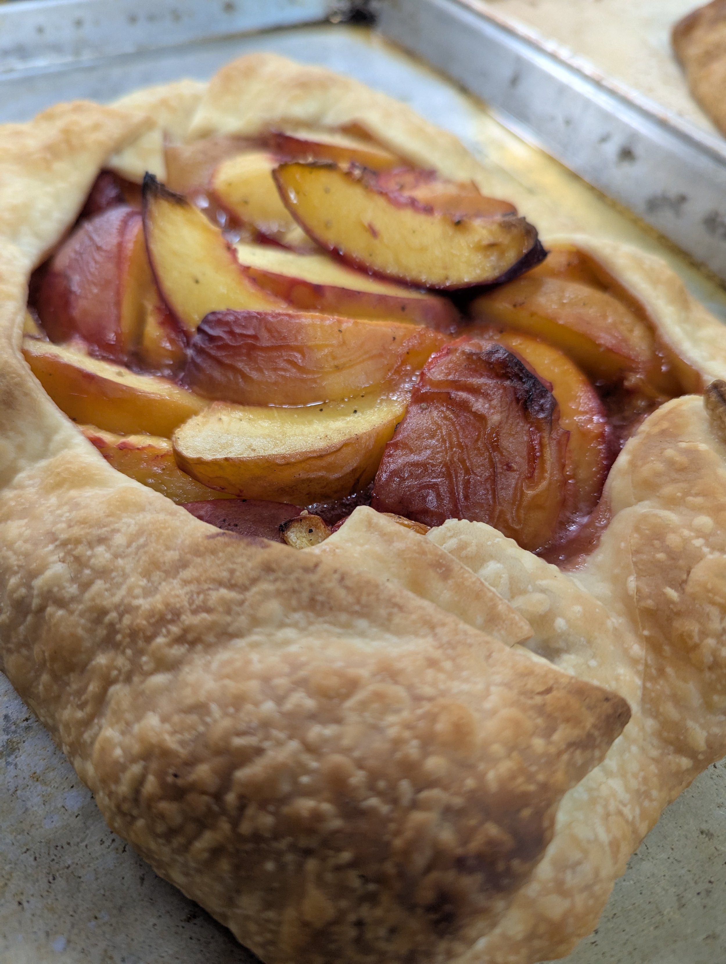 Fresh peach galette with a flaky crust and sliced peaches inside on a baking sheet.