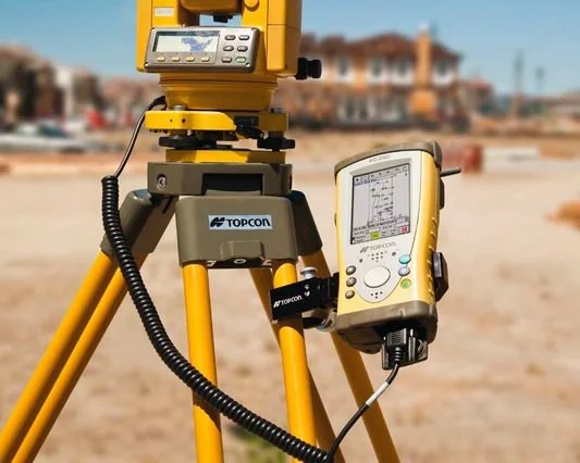 Surveyor's tripod with a total station and a data collector on a construction site.