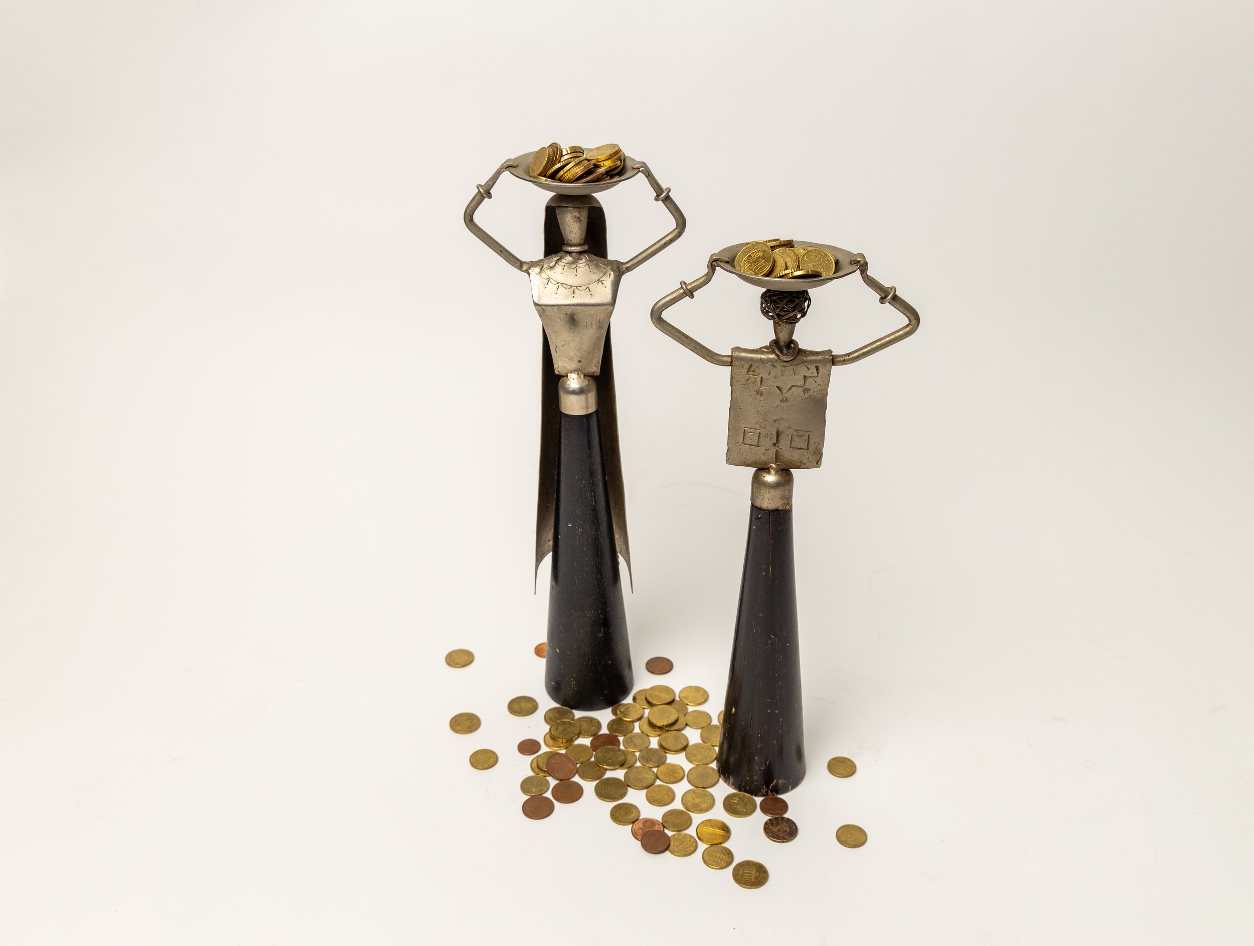 Decorative sculptures of metal figures holding bowls of coins, with coins scattered at the base, against a plain white background.