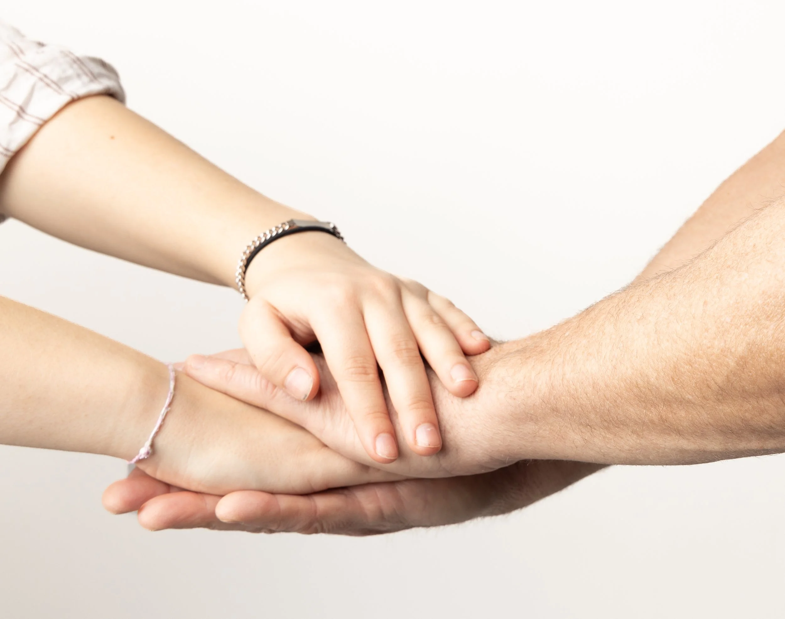 Two people holding hands in a supportive gesture; one person has a light skin tone and the other has a darker skin tone; the person with lighter skin wears bracelets.