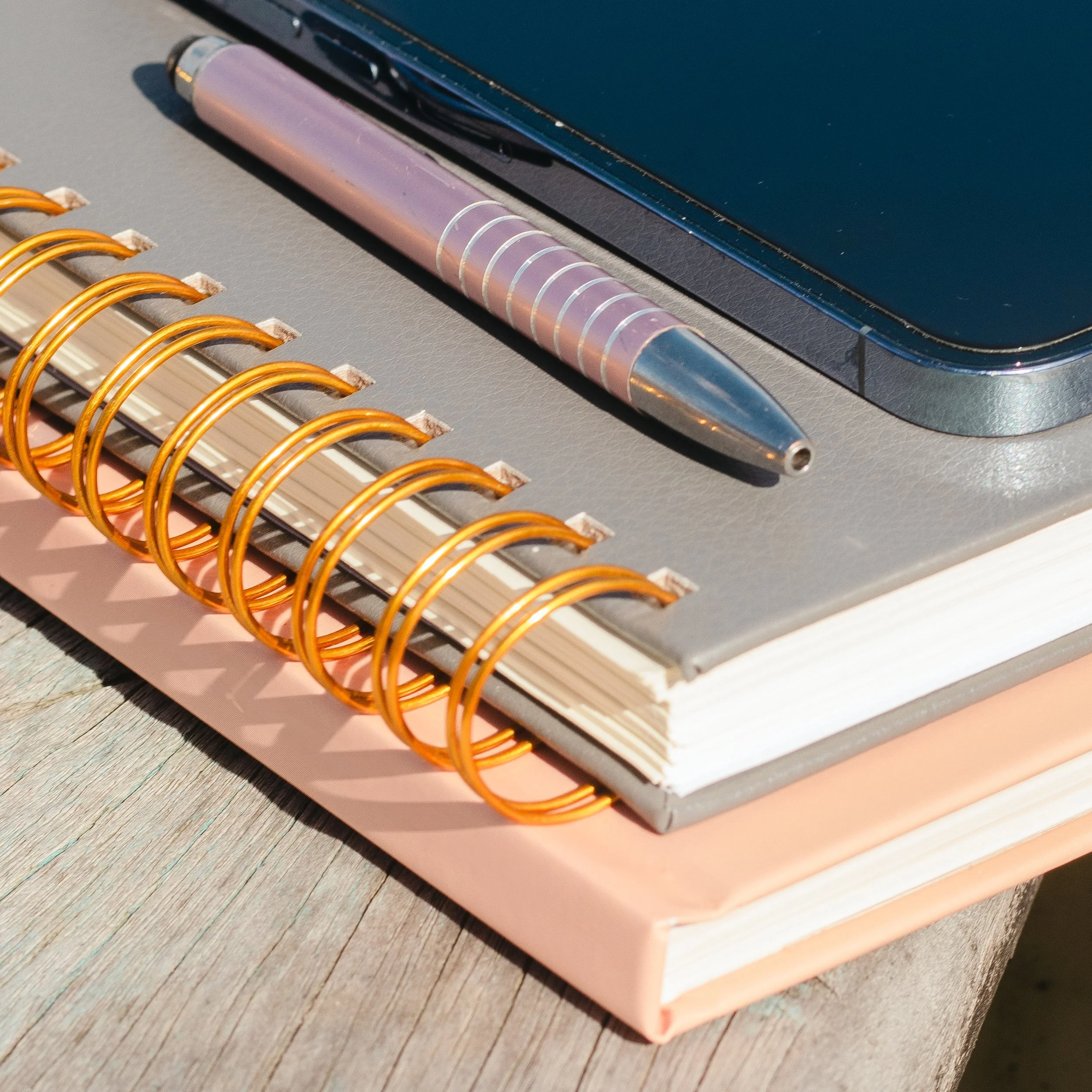 Stacked notebooks with a spiral binding, a pen, and a phone on top.