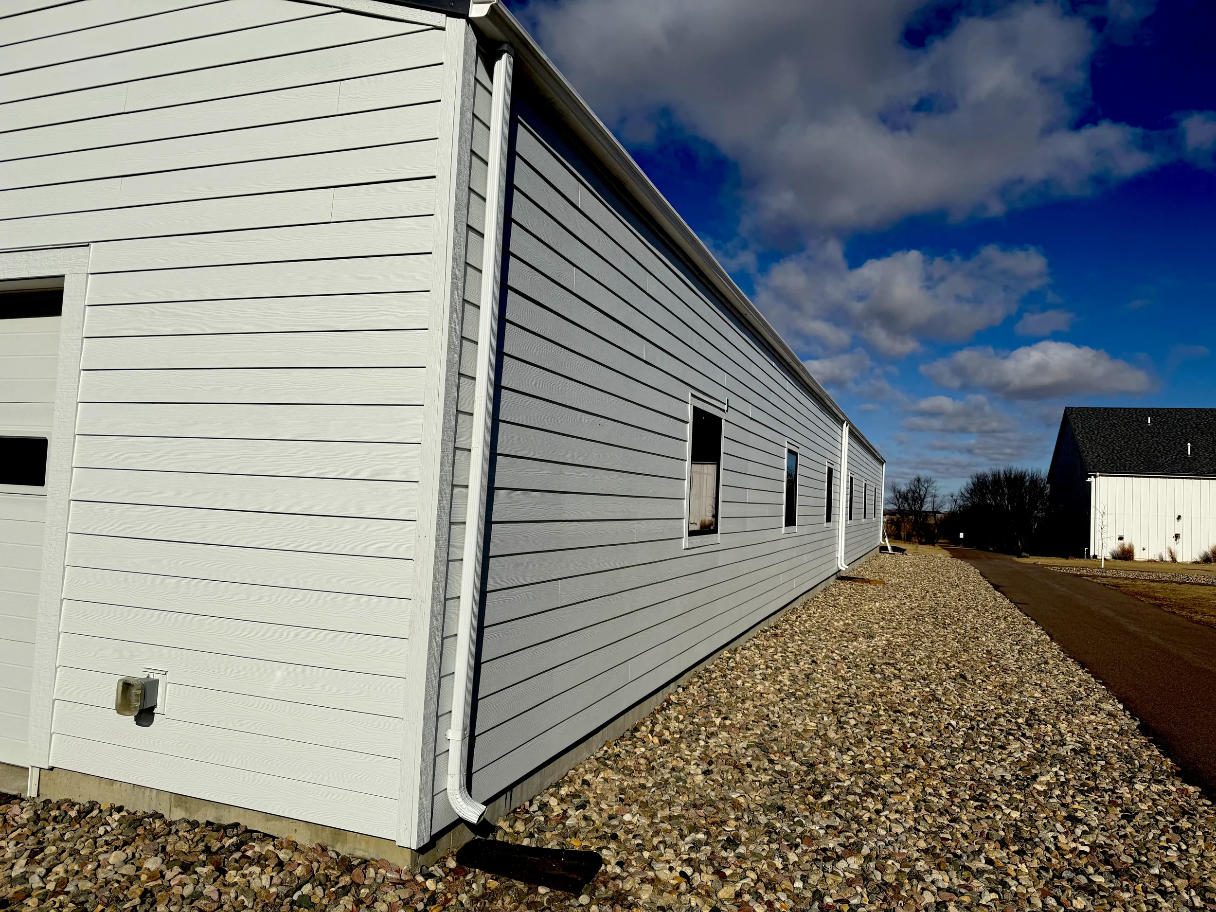 Exterior of a white residential building with horizontal siding, four small windows, a door, and a gutter system, under a partly cloudy sky.