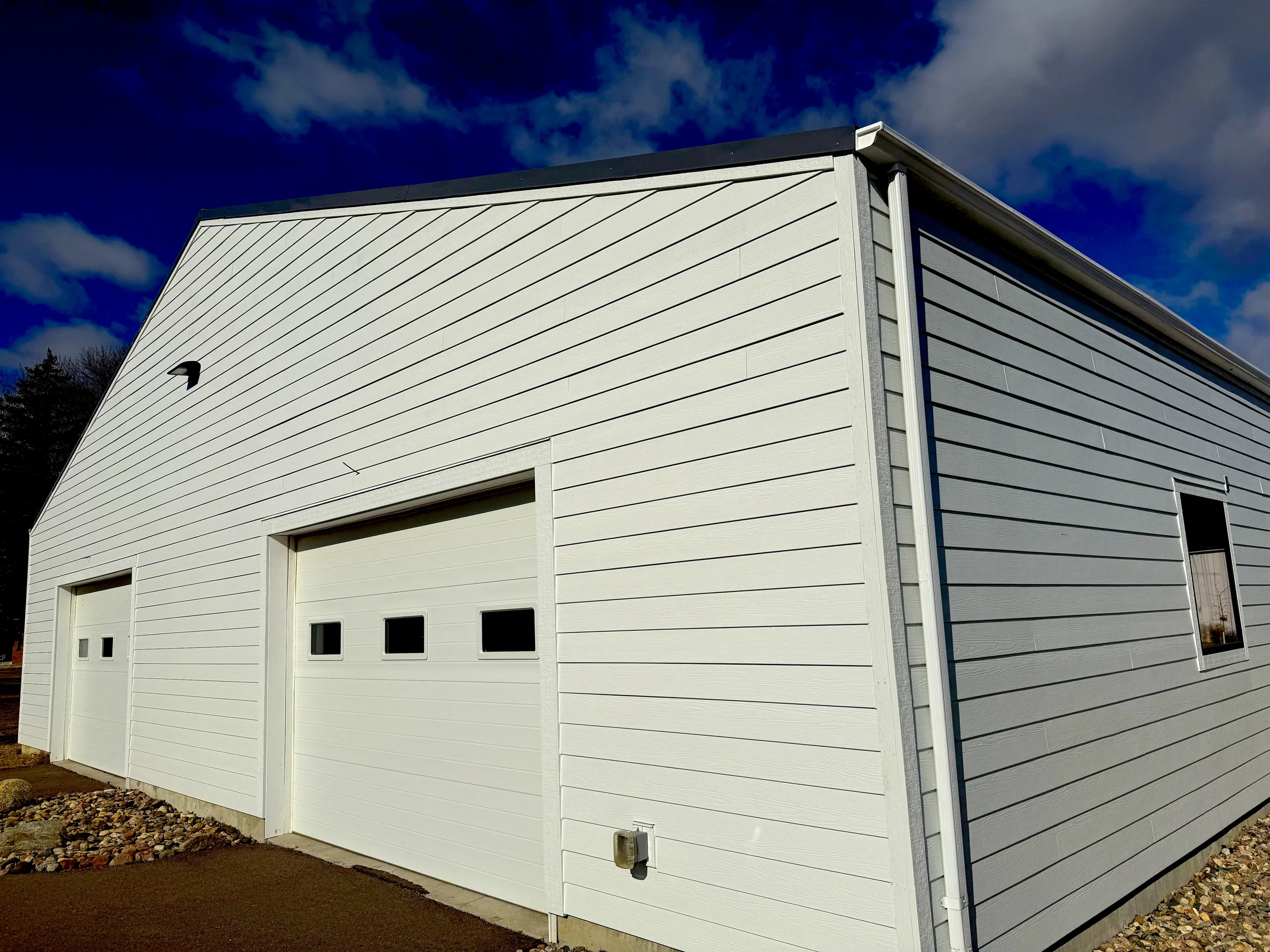 White barn-style building with three garage doors and a window, under a partly cloudy blue sky.