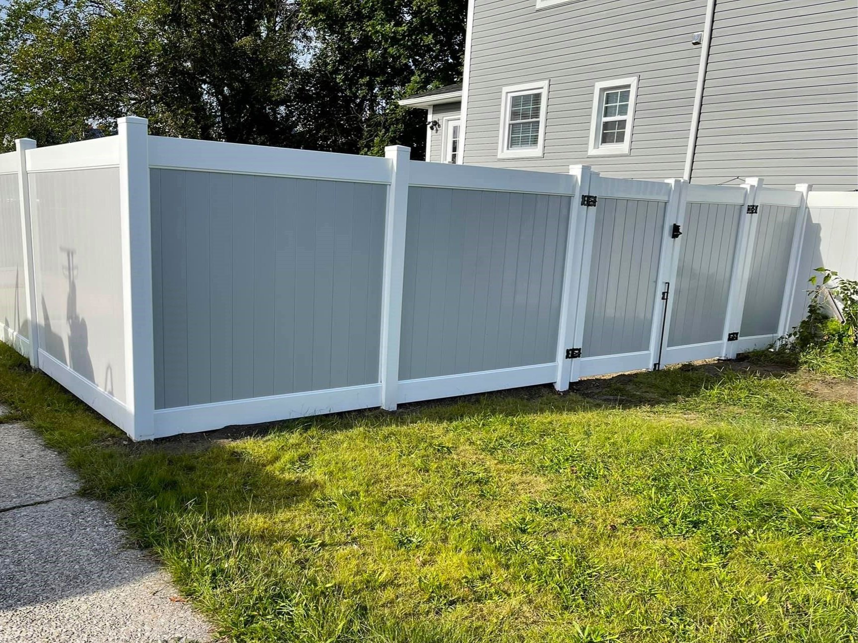 Gray and white vinyl privacy fence with green grass and a house in the background.