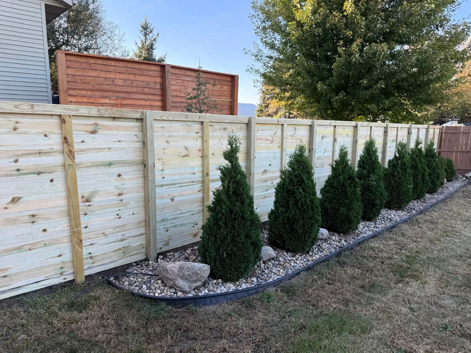 Horizontal wood fence with modern landscaping and decorative trees.