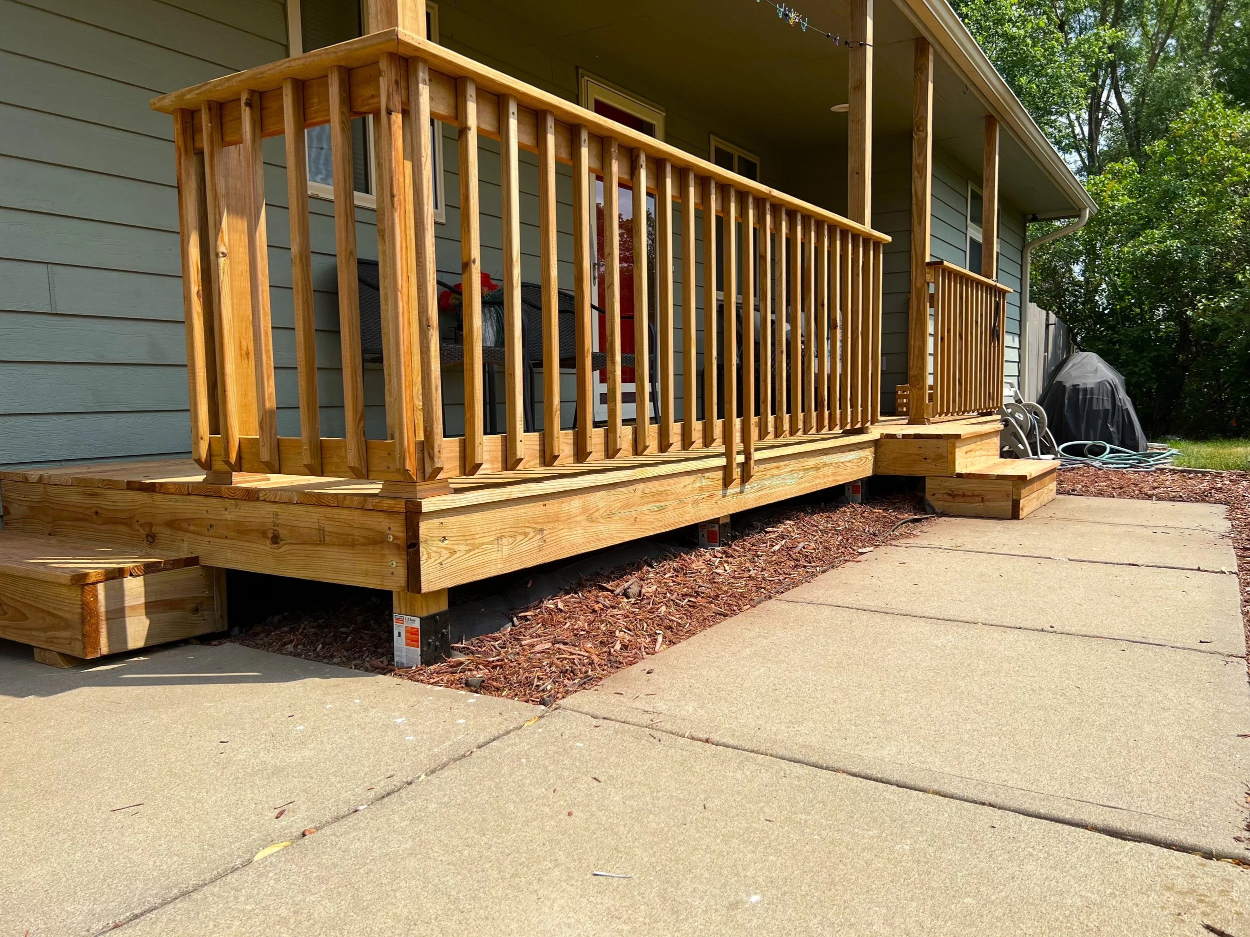 Front porch style wood deck with railing and concrete walkway in Sioux Falls