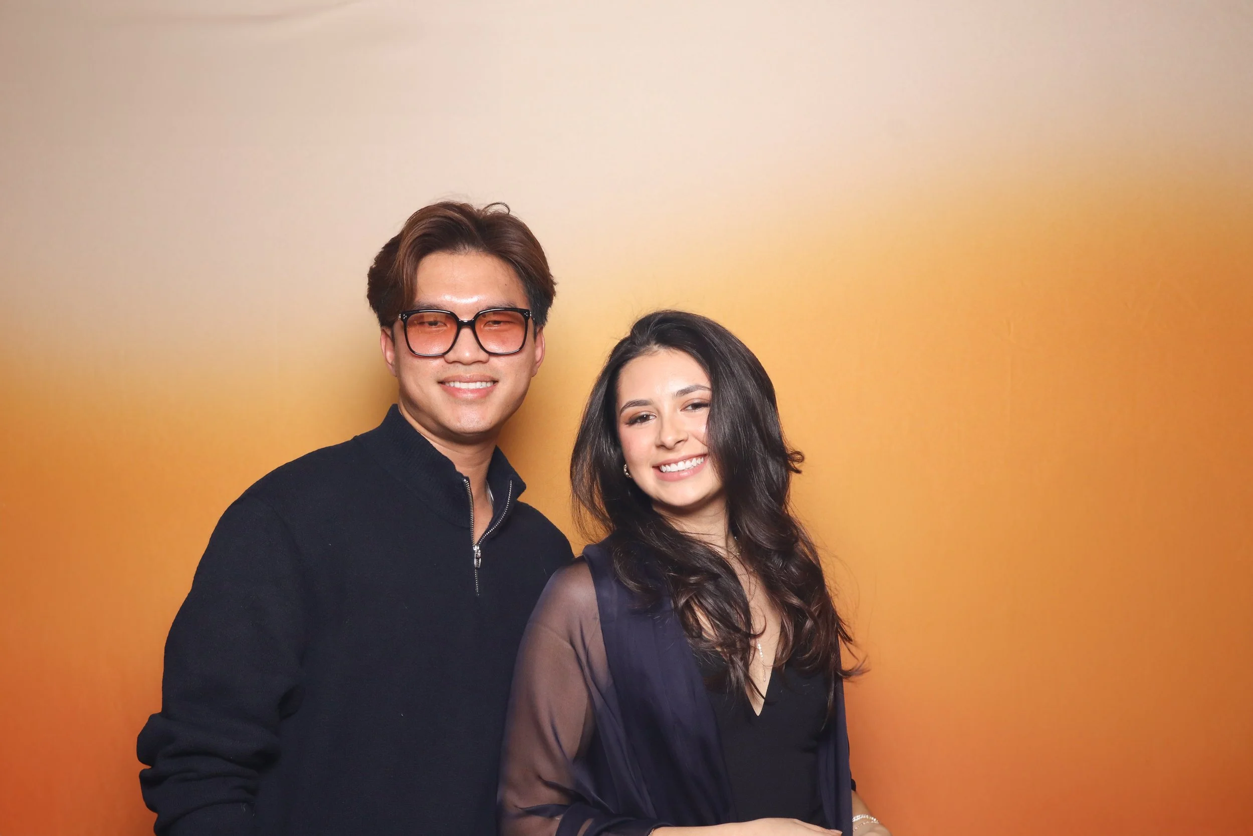 Two people smiling against an orange gradient background.