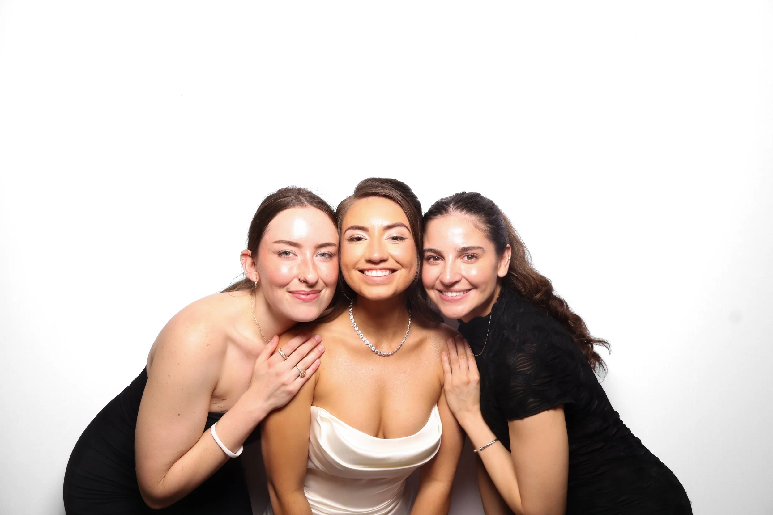 Three women smiling and hugging against a plain white background.