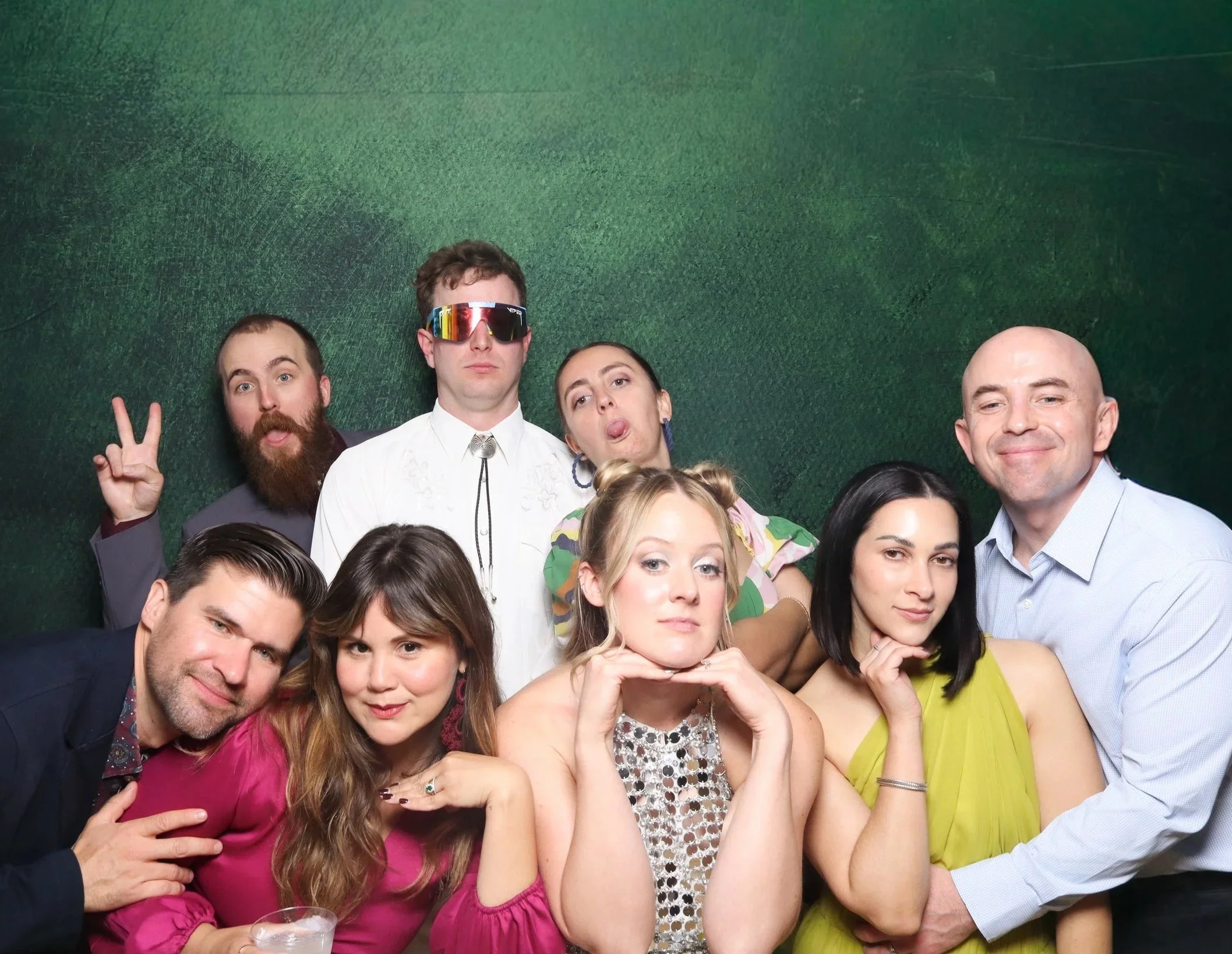 Group of people posing for a photo at a party, with a green textured wall in the background.