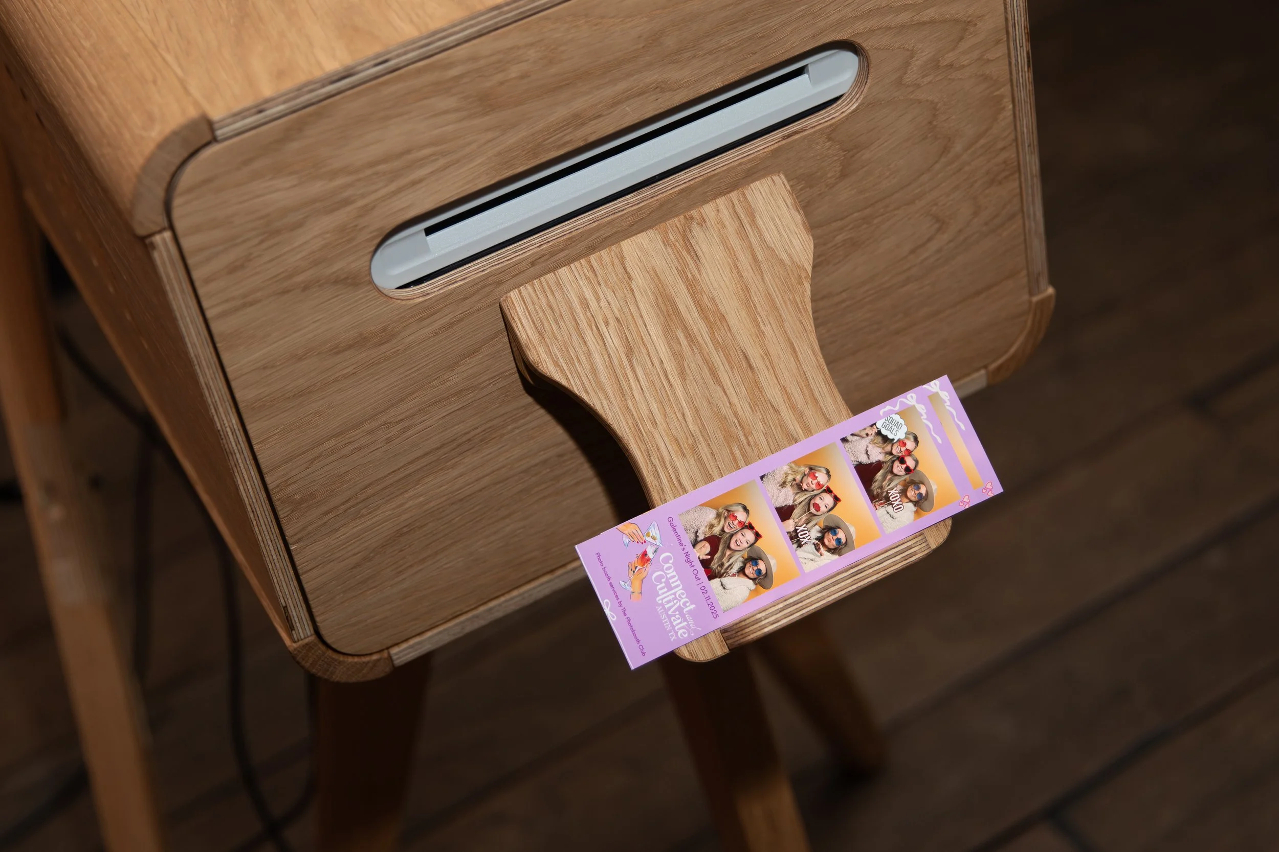 Wooden photo booth printer with a printed photo strip featuring people wearing sunglasses.