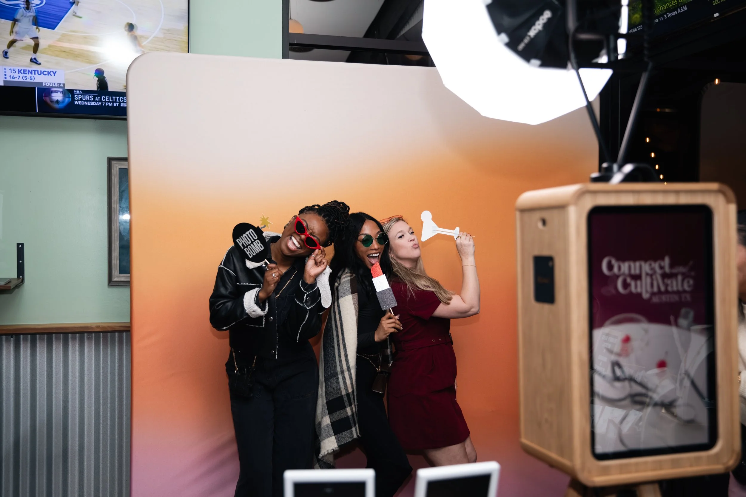 Three people posing in a photo booth with props and an orange backdrop.