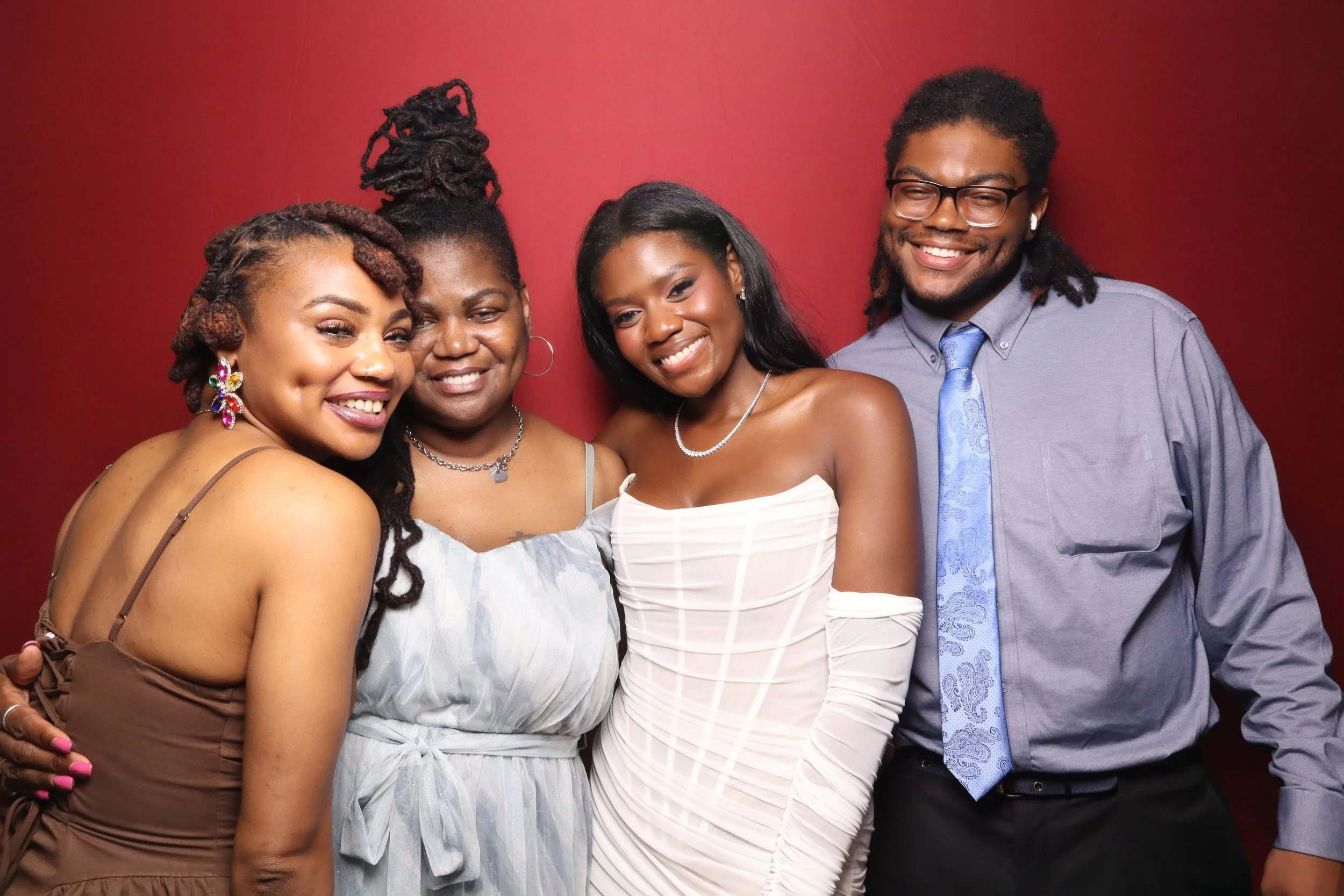 Four diverse friends posing together against a red background, smiling and embracing each other.