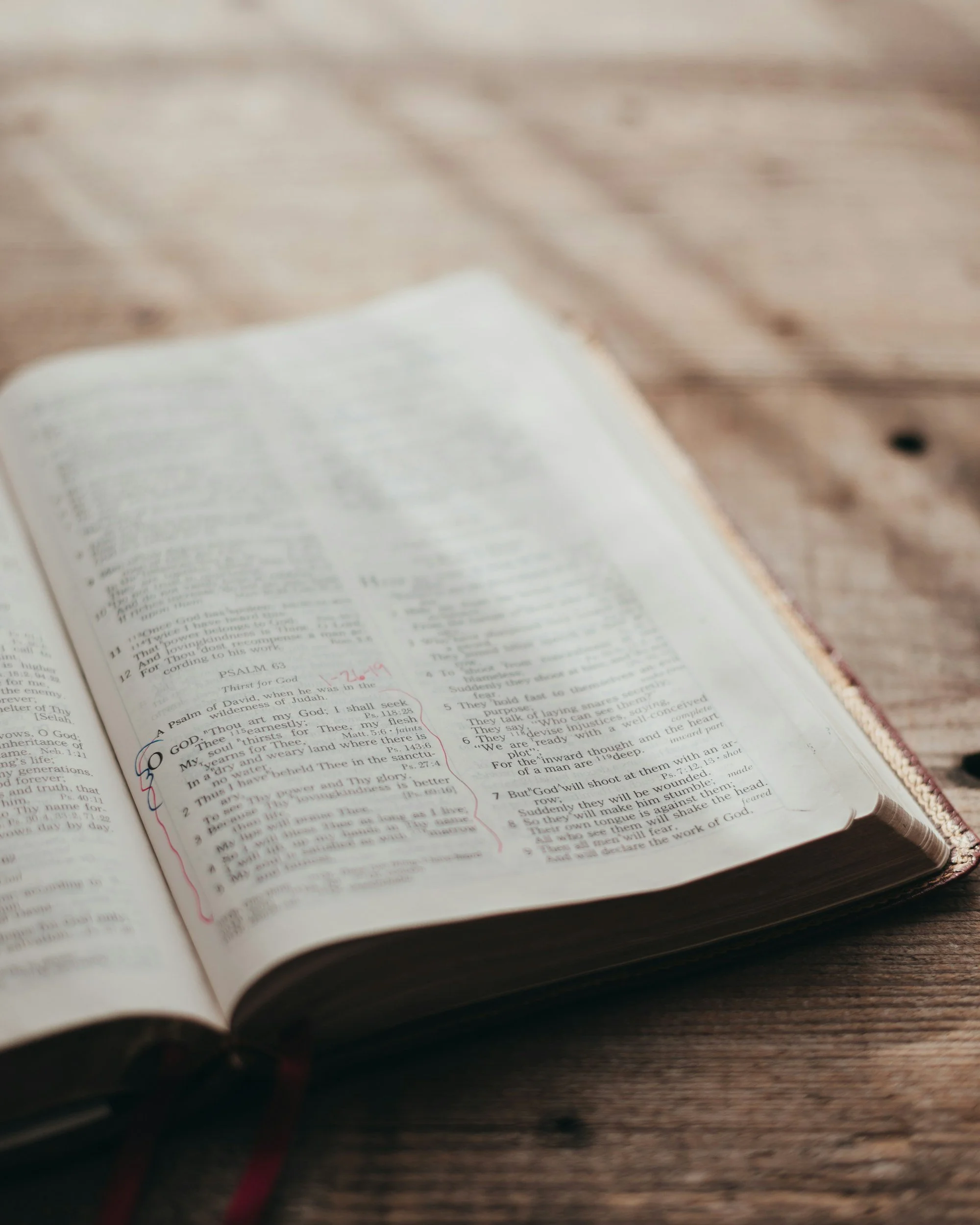 Open Bible on a wooden table with handwritten notes and markings.