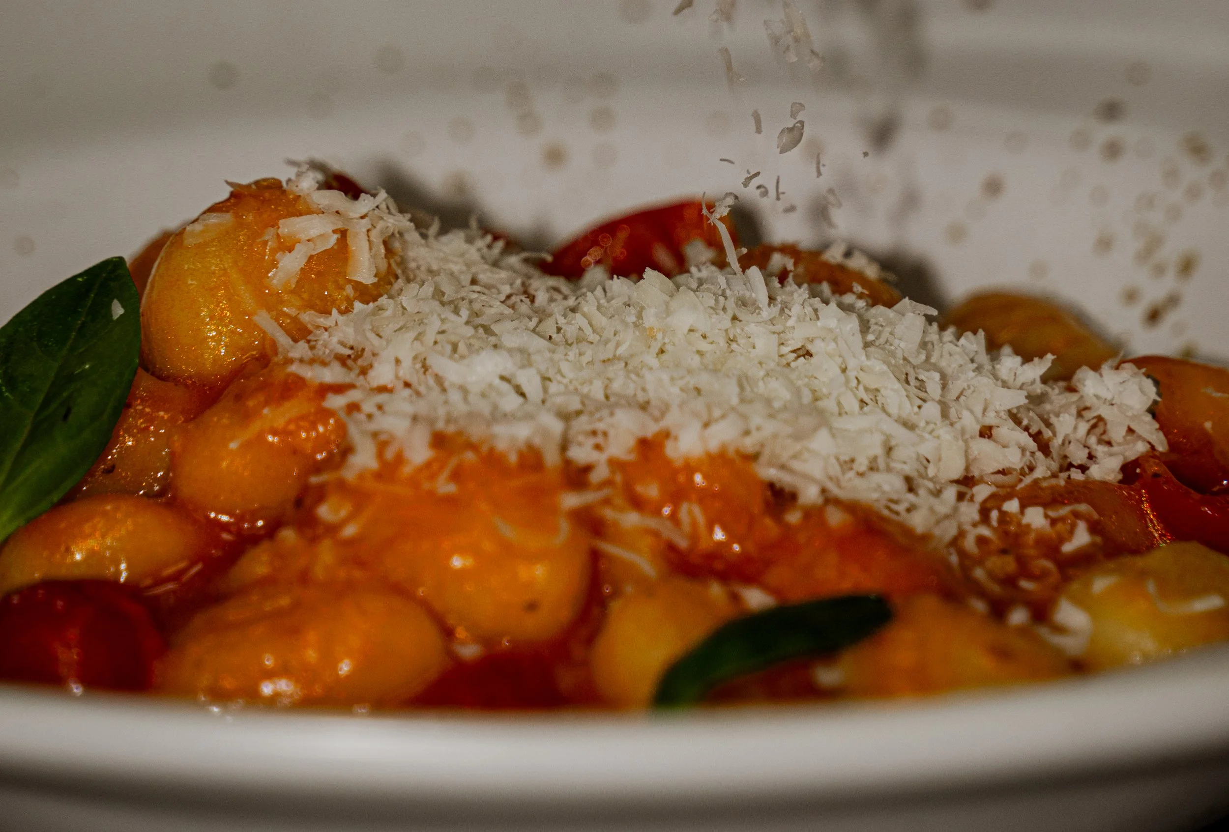 Plato de pasta con salsa de tomate, queso rallado y hojas de albahaca.