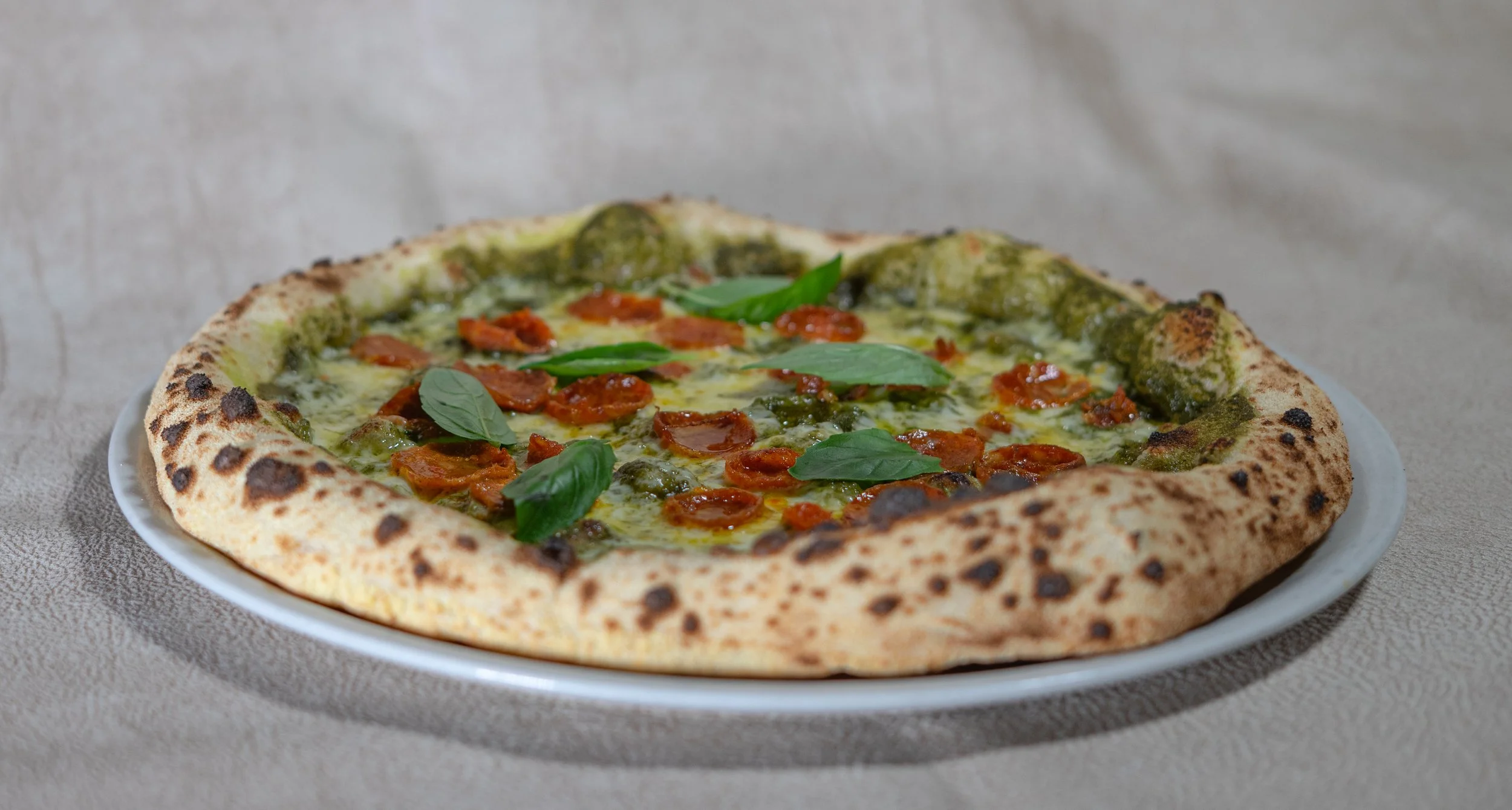 Pizza de masa artesanal con salsa, tomate, aceitunas y hojas de albahaca encima en un plato blanco