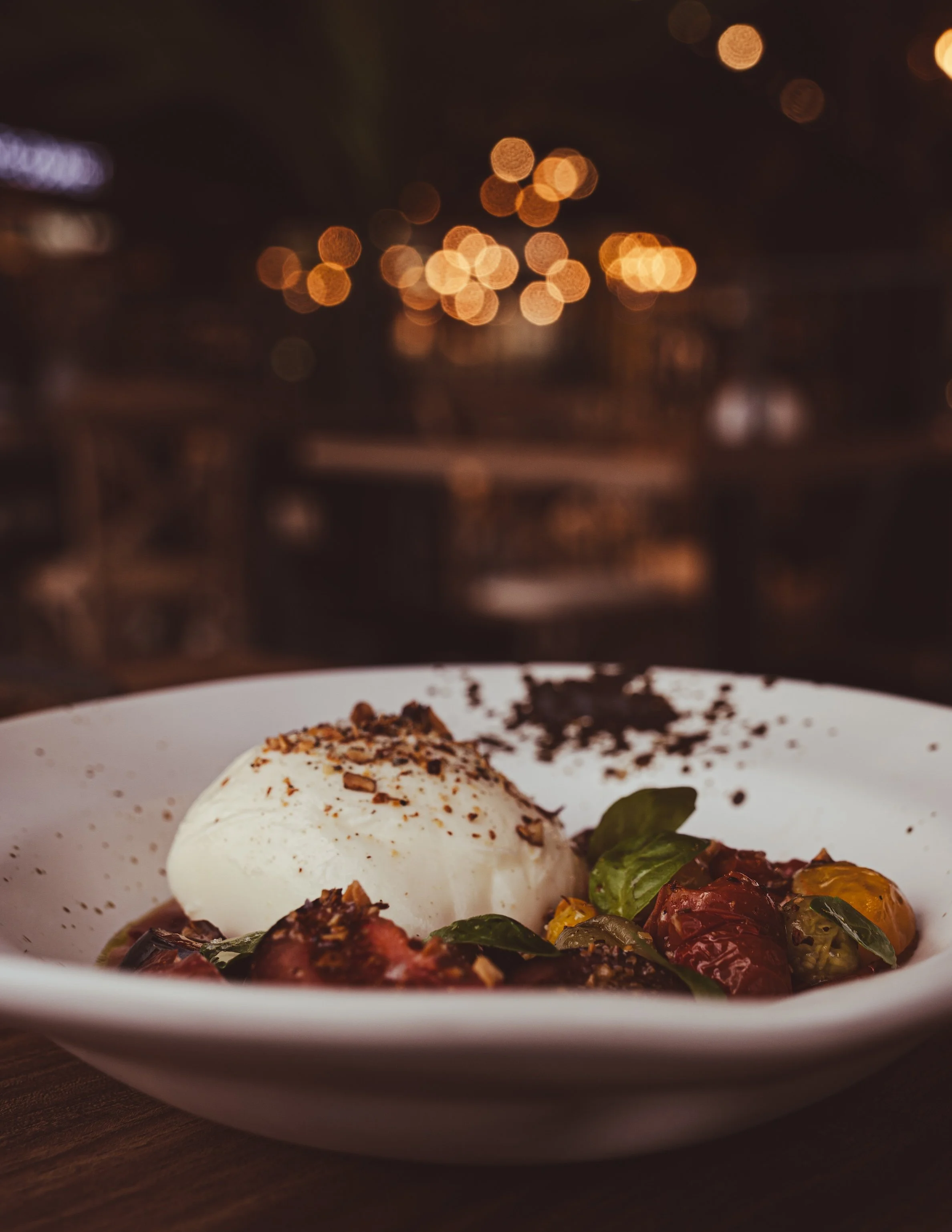Plato de ensalada con vegetales asados, burrata y hierbas frescas en un fondo nebuloso con luces térmicas cálidas.