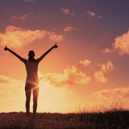 Silhouette of person with arms raised in field at sunset. Prodigal Heroes Community