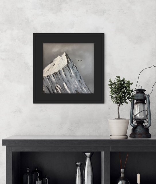 Framed artwork of a snow-capped mountain on a wall above a console table with a potted plant, lantern, and decorative objects.