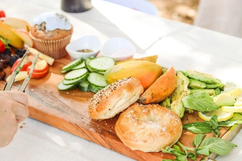 Detail shot of breakfast spread, including fresh bagels, fruits and veggies, and pastries.