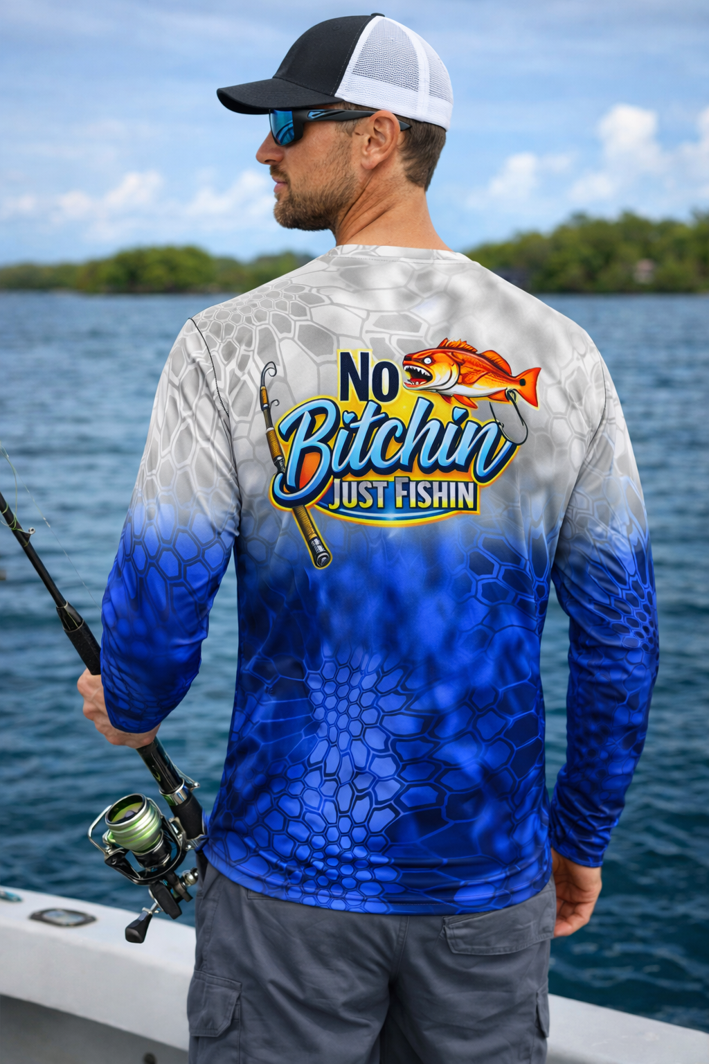 Man fishing on a boat, wearing sunglasses, a baseball cap, and a blue and white fishing jersey that says, "No Bitchin Just Fishin," with a fish graphic.