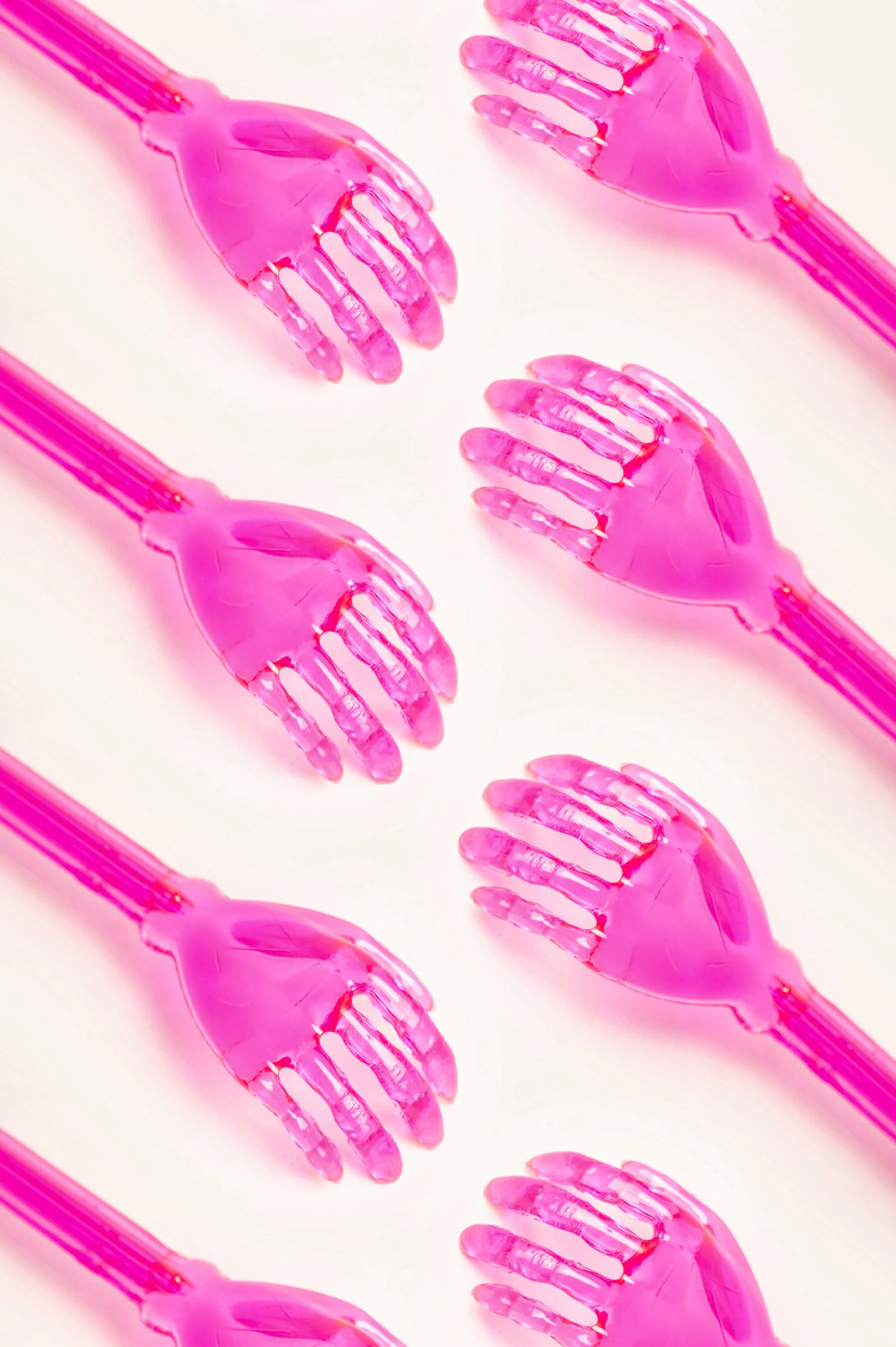 Multiple pink plastic hand-shaped spatulas arranged parallel on a white surface.