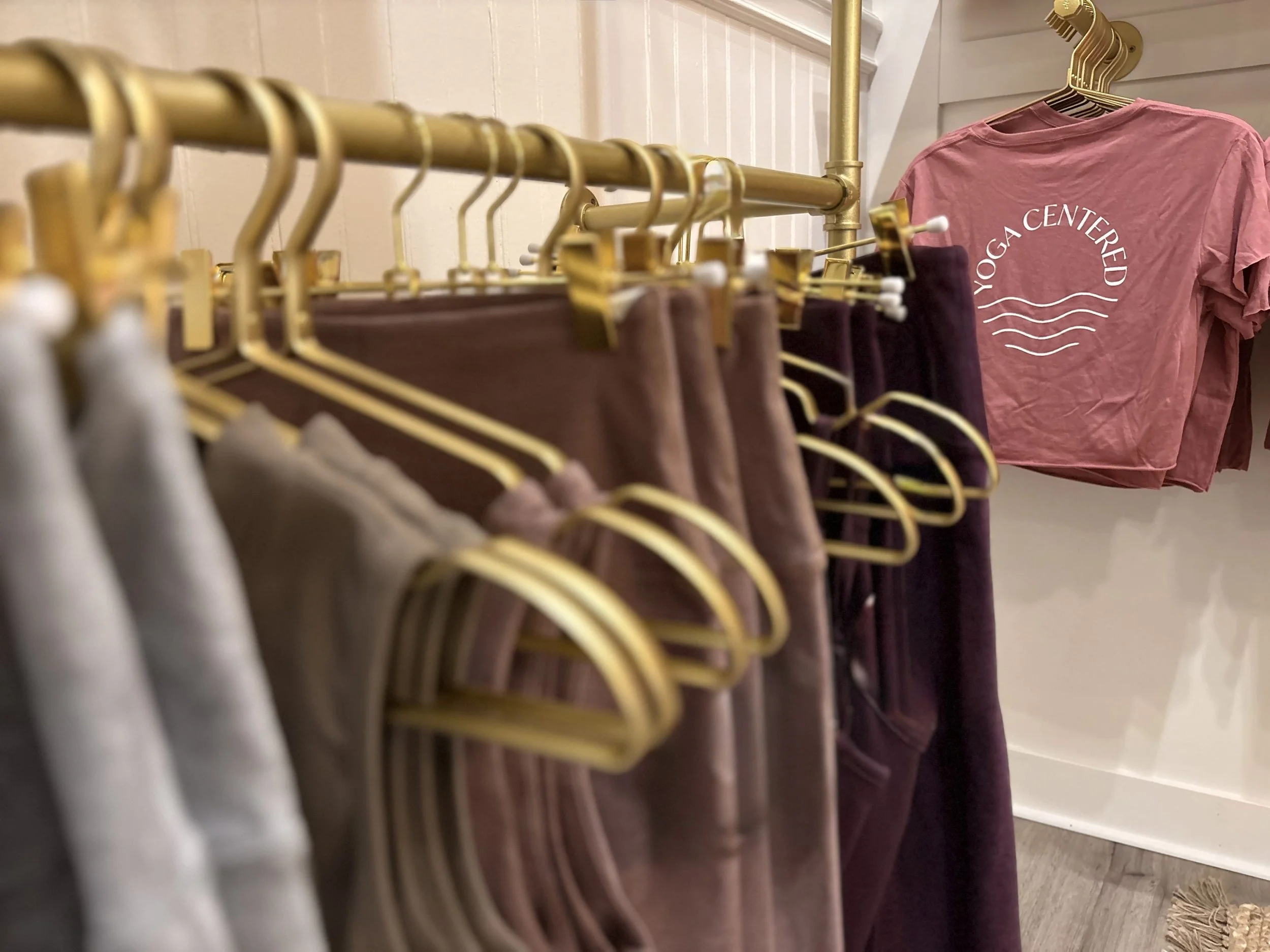 Clothing rack with folded sweatshirts and a pink t-shirt that reads 'YOGA CENTERED' in the Yoga Centered Boutique Big Island, Hilo