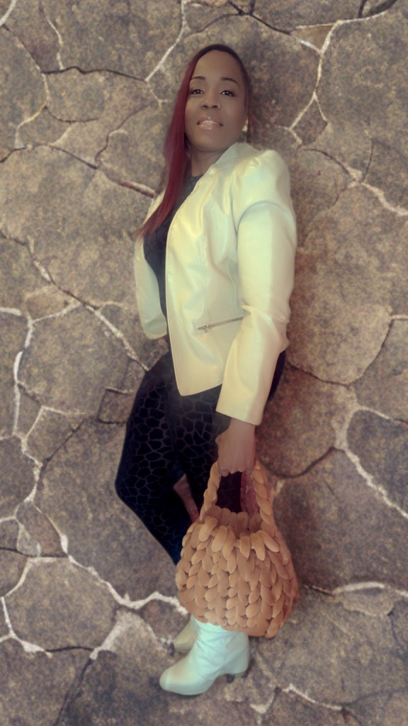 Person posing in a white jacket and holding a textured bag, standing against a cracked stone wall background.