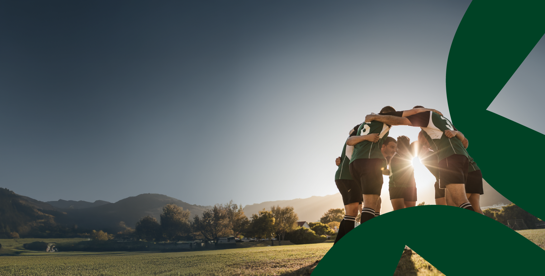 A rugby team huddled together on a field during sunset, preparing for a game with mountains in the background representing Collaborate for success with a joint business plan