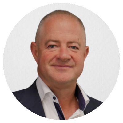 A man in a navy suit jacket and white shirt standing against a dark background.
