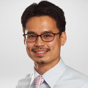 Portrait of a smiling man wearing glasses, a white dress shirt, and a pink patterned tie.