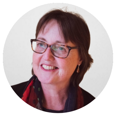 A middle-aged woman with short brown hair and glasses smiling indoors.
