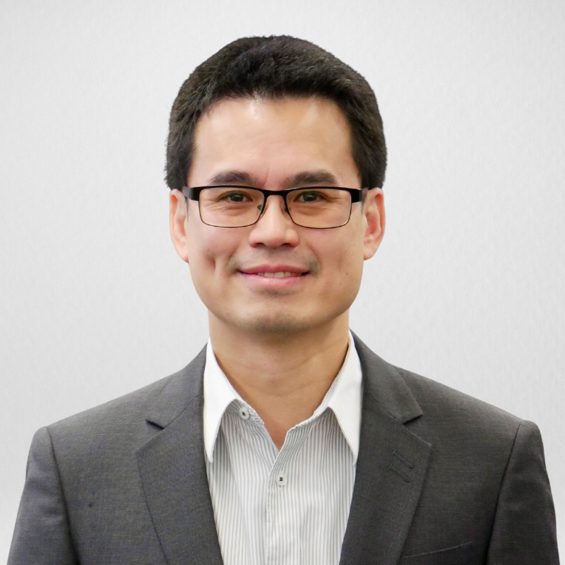 Portrait of a smiling man wearing glasses, a white dress shirt, and a pink patterned tie.