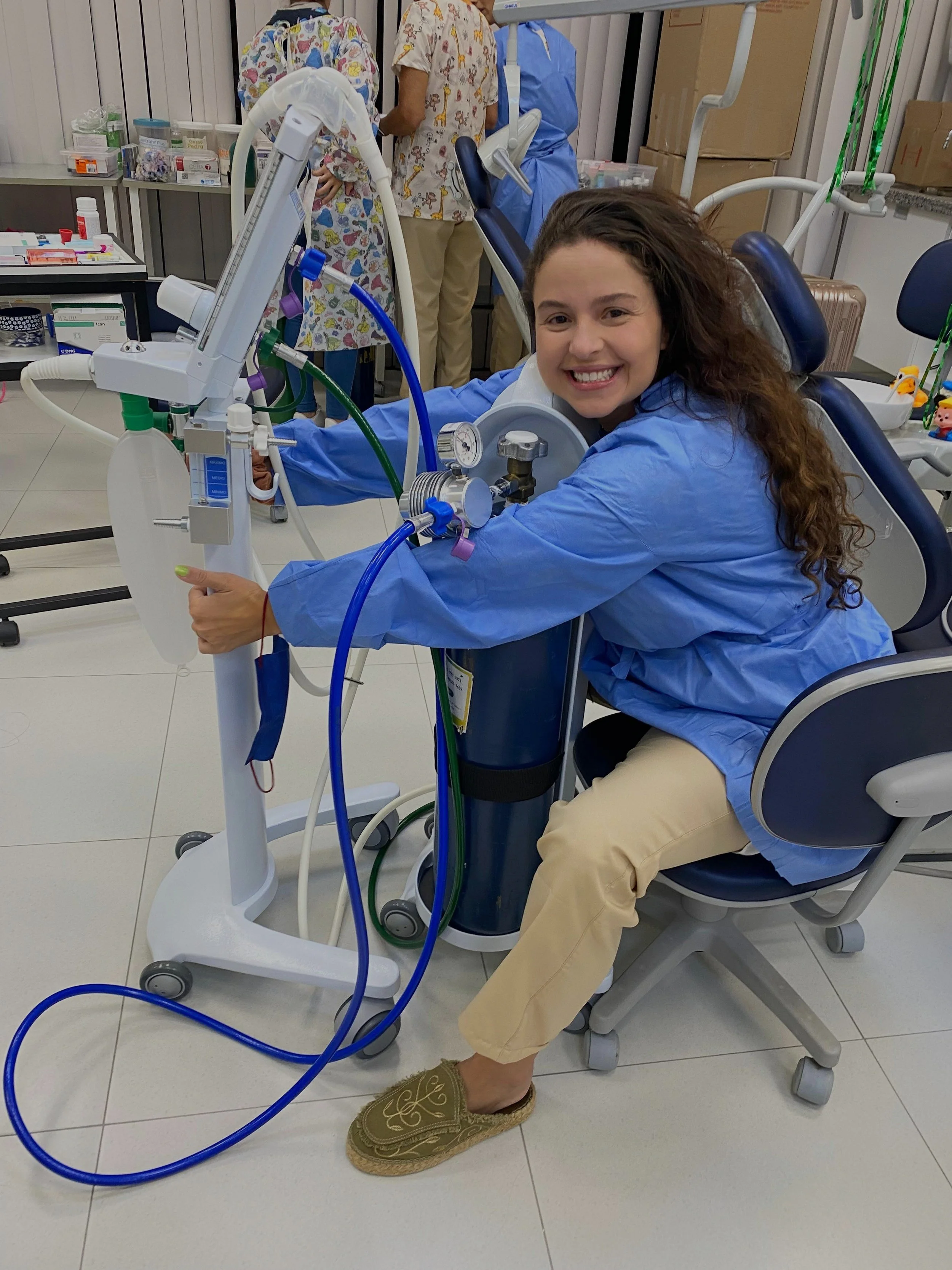 Mulher sorridente sentada em cadeira ao lado de equipamento médico em consultório odontológico.