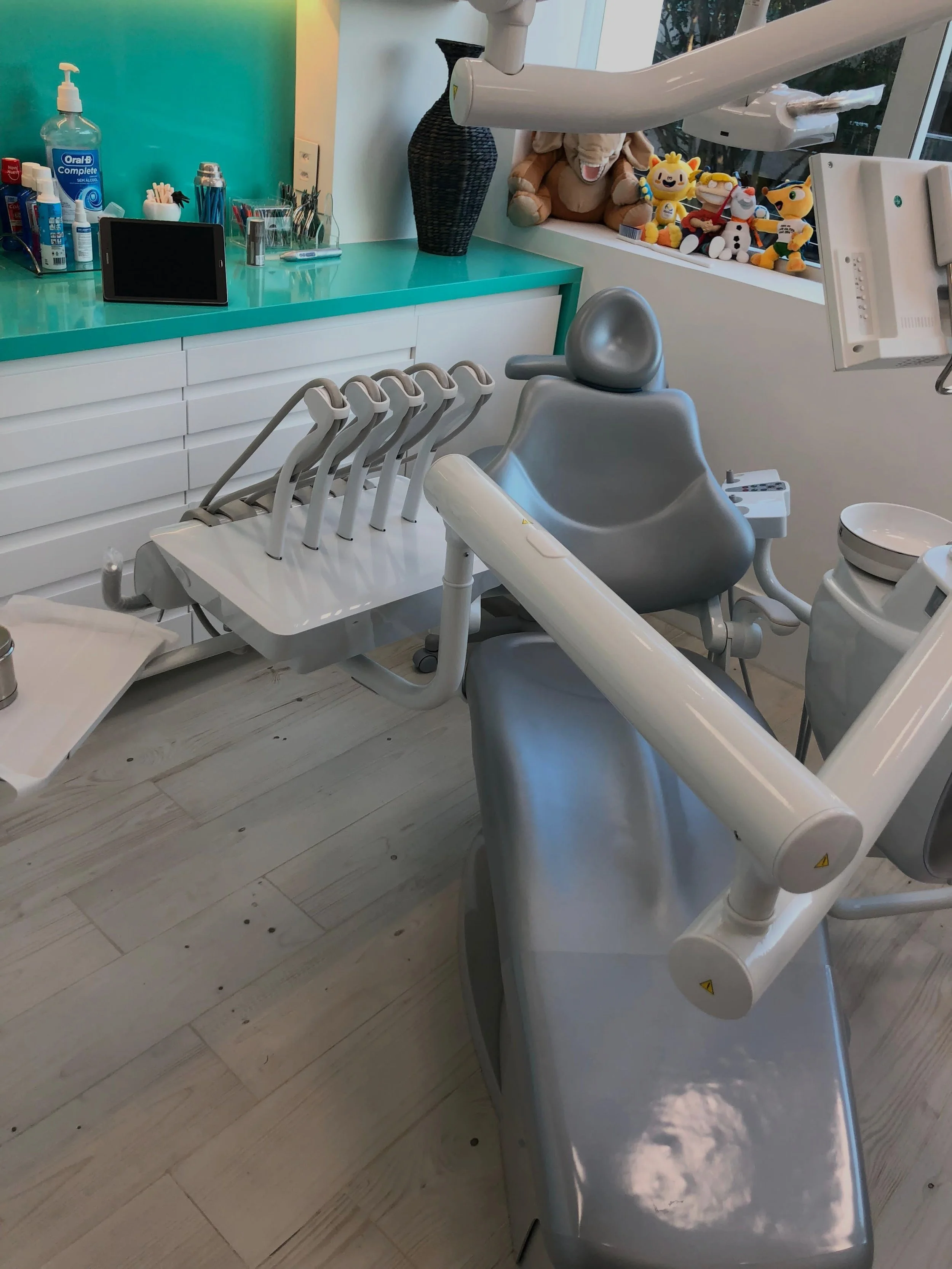 Consultório odontológico com cadeira de dentista, instrumentos odontológicos e brinquedos decorativos ao fundo.