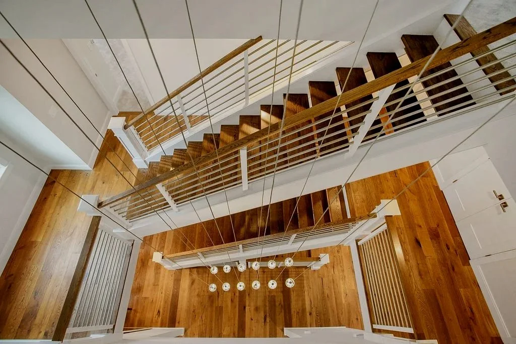 From the top view of a staircase, showing wooden steps, white railing, and a modern chandelier hanging from the ceiling with multiple bulbs.