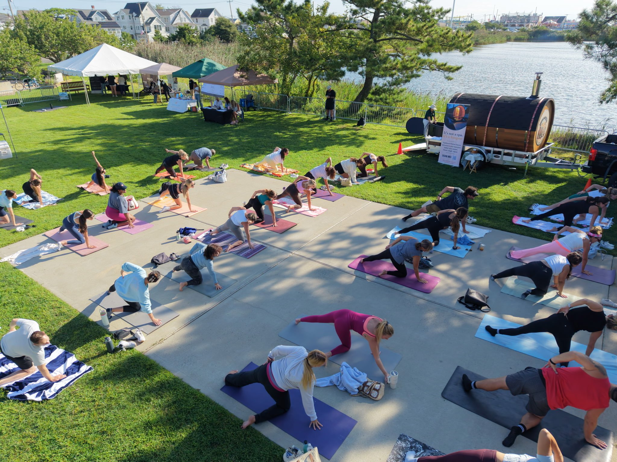 People practicing outdoor yoga on mats near a river, with tents and trees in the background.