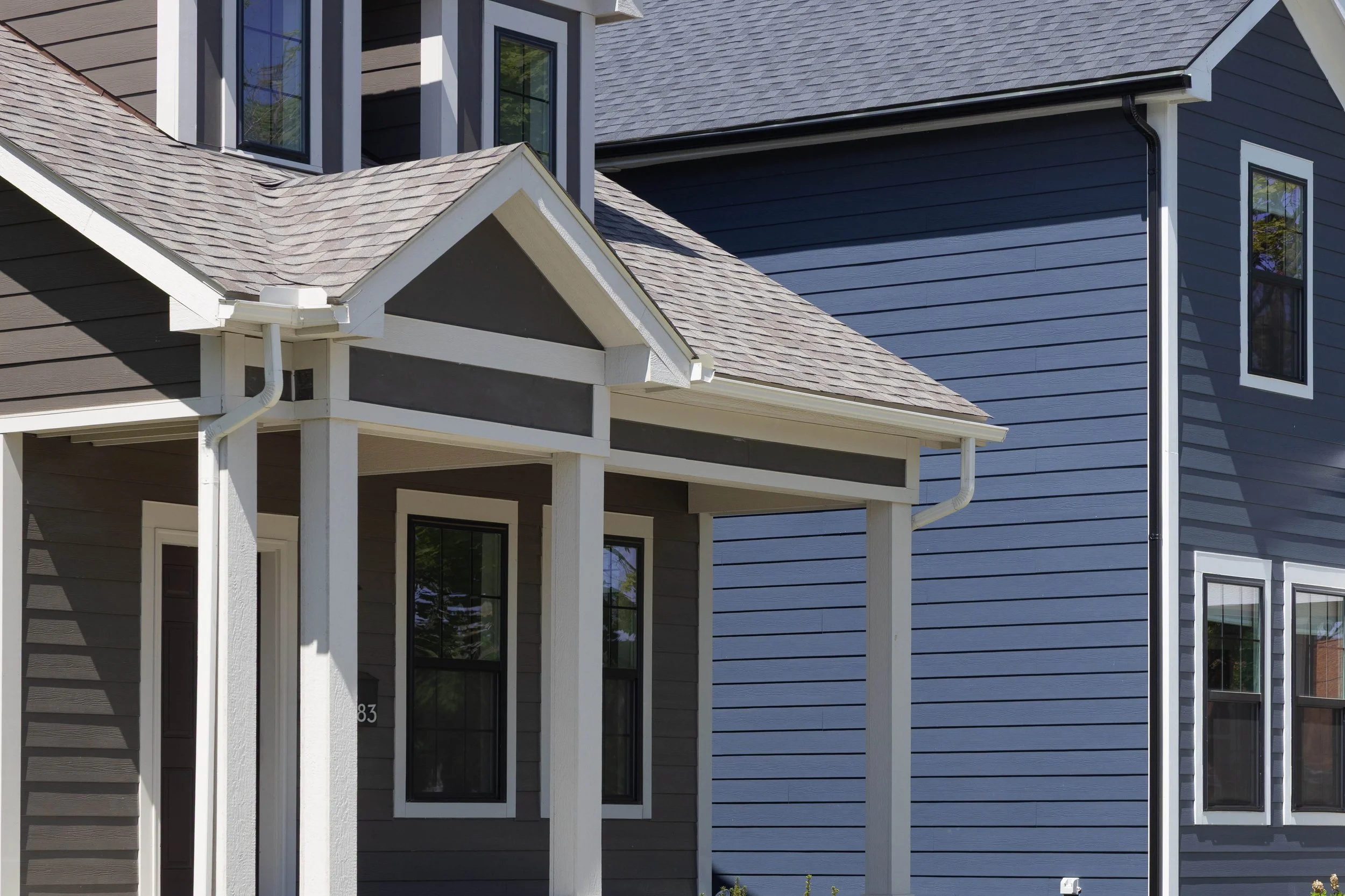 Close-up of the exterior of a new construction house in detroit featuring grey and blue siding, white trim, and a small porch with columns.